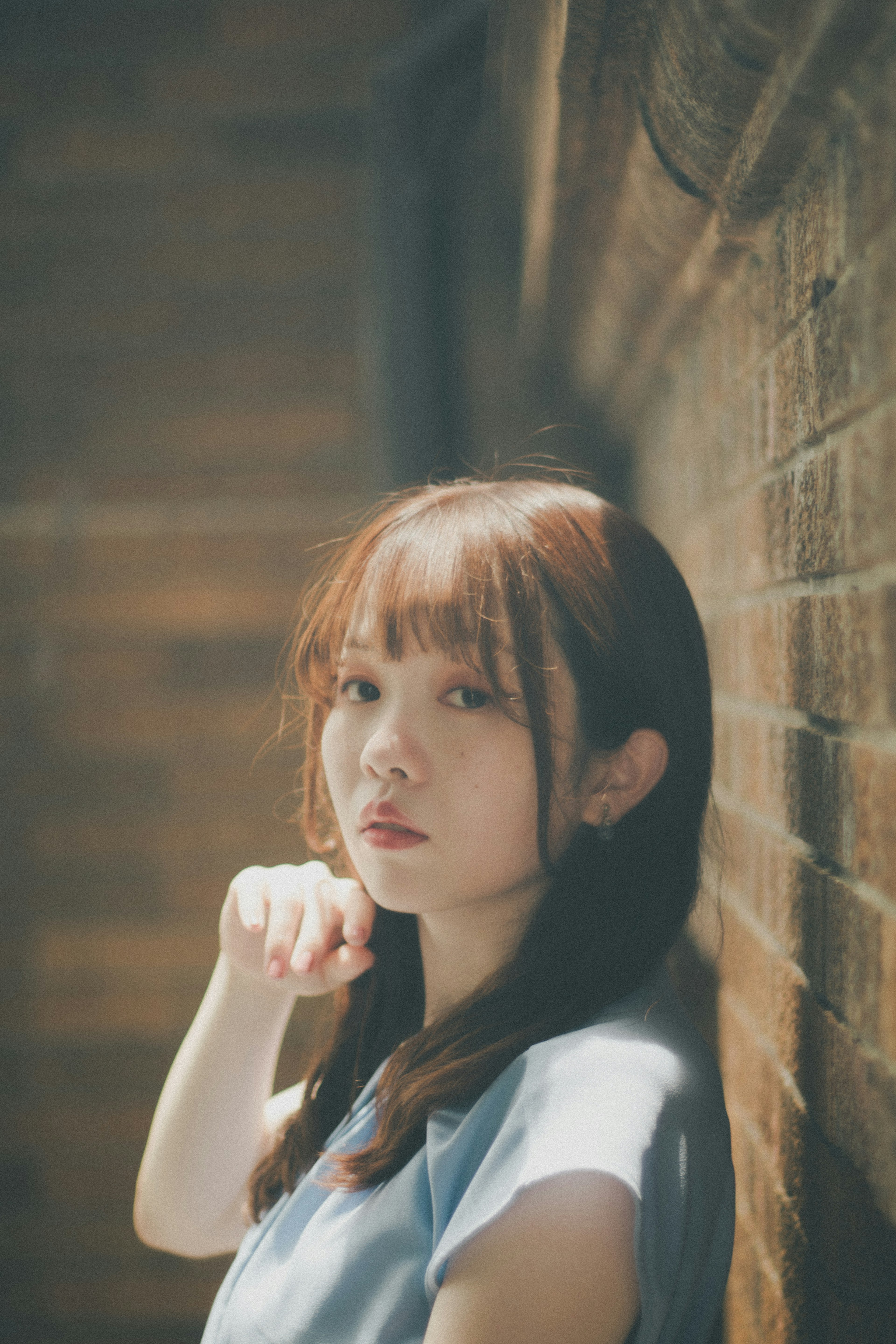 Portrait of a woman leaning against a wall Soft natural light Brown hair Simple colored clothing