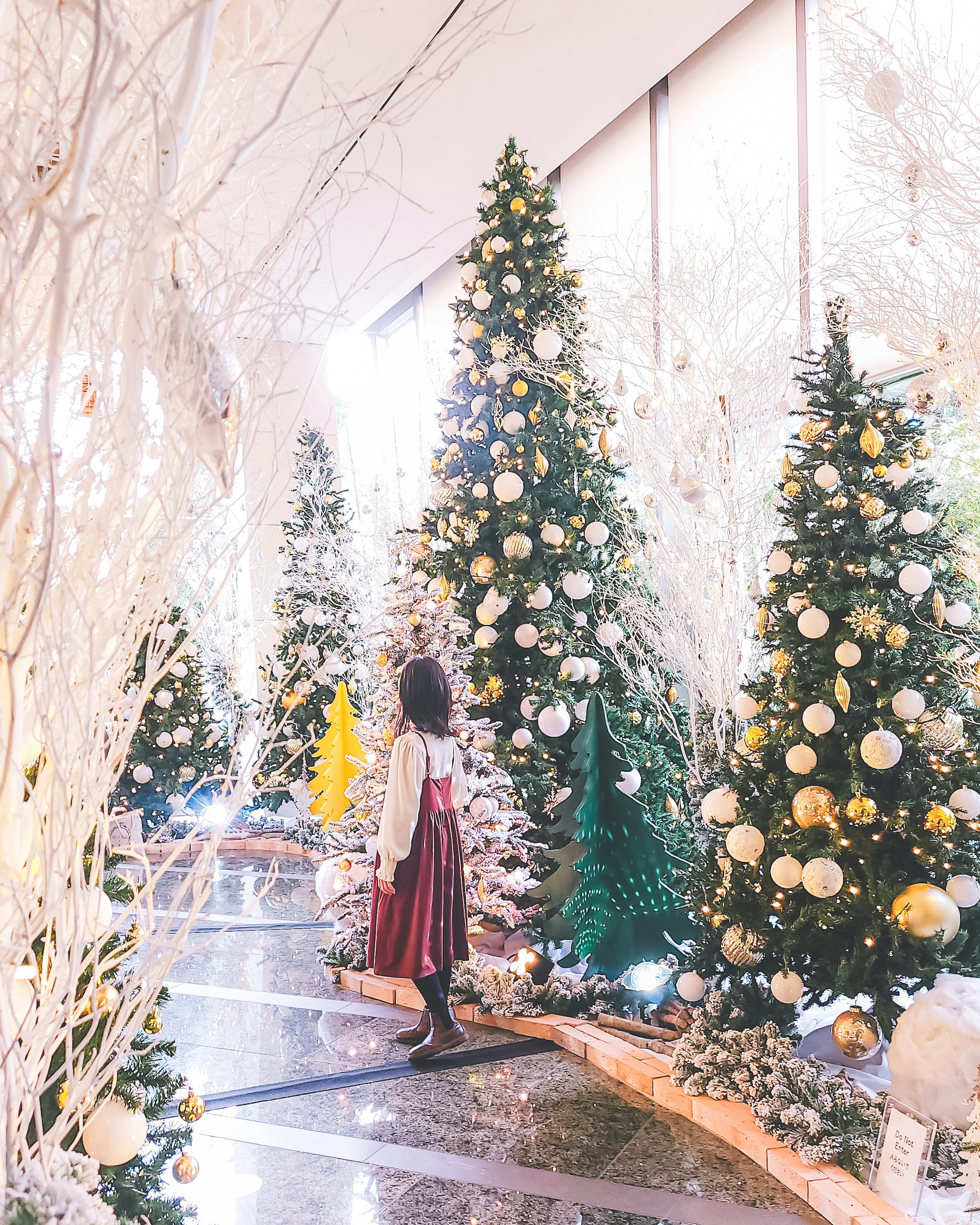 Una niña de pie en un pasillo brillante rodeada de árboles de Navidad decorados