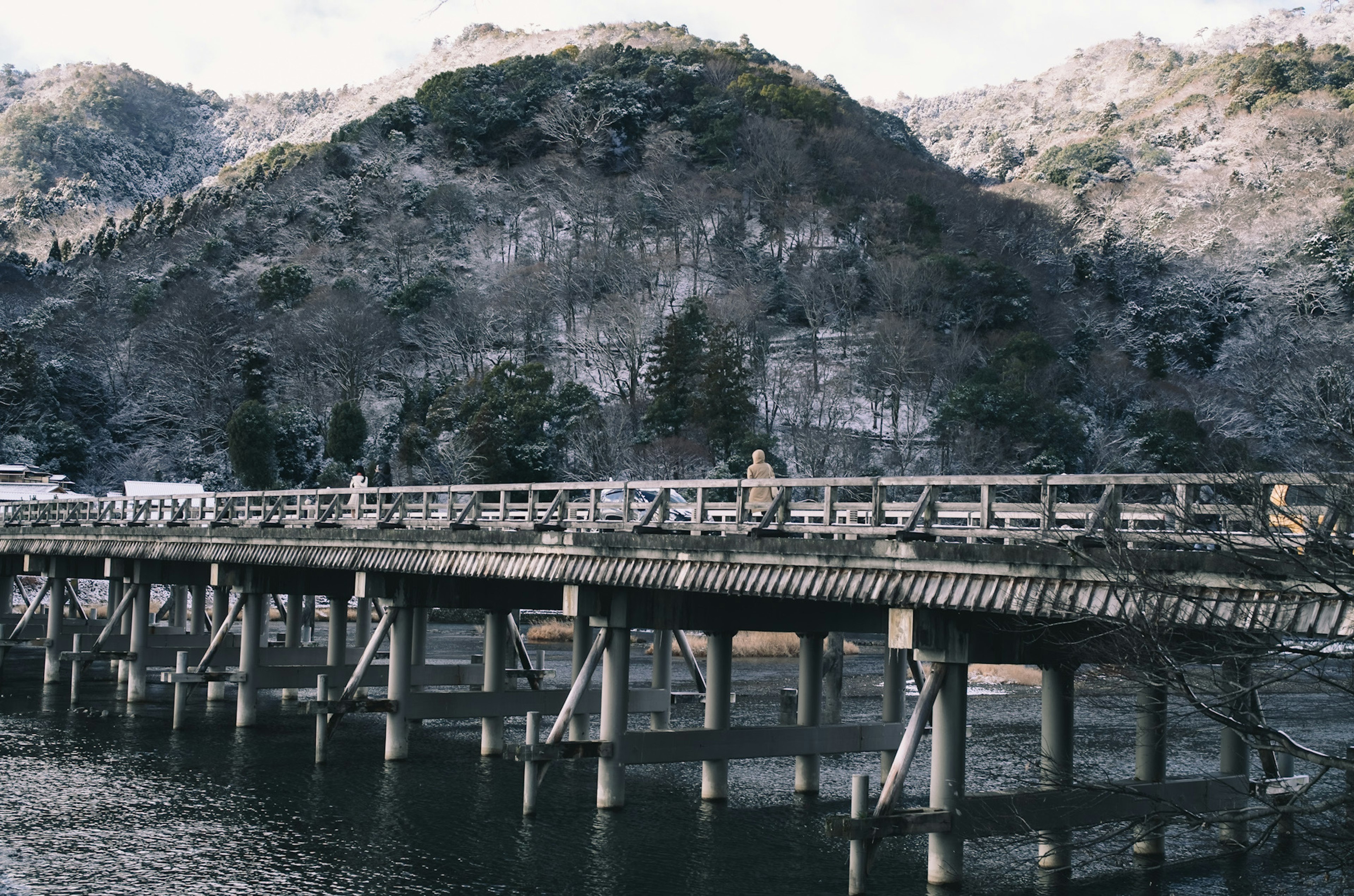 冬の山々を背景にした木製の橋が川にかかっている