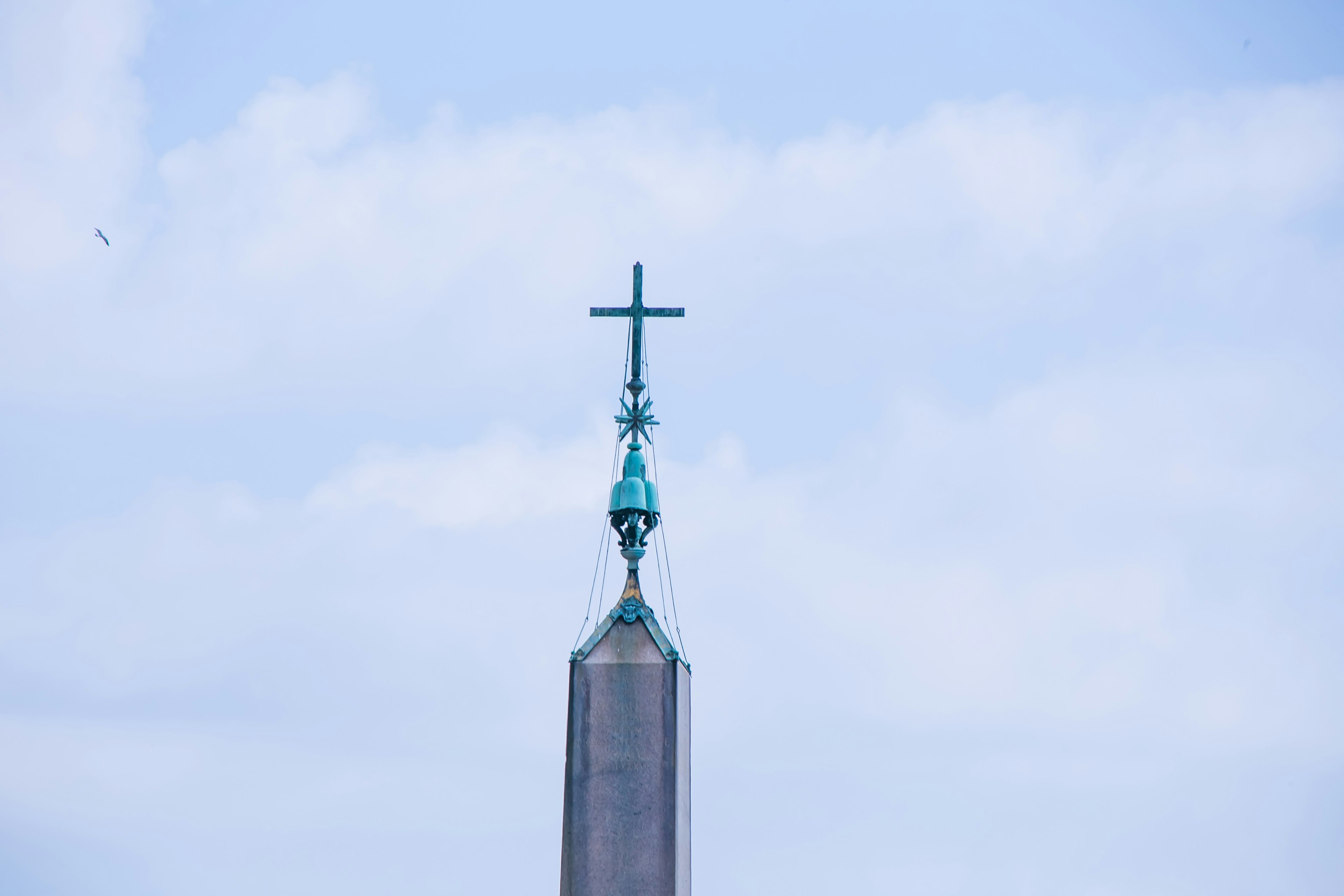 Top of a spire featuring a cross against a blue sky