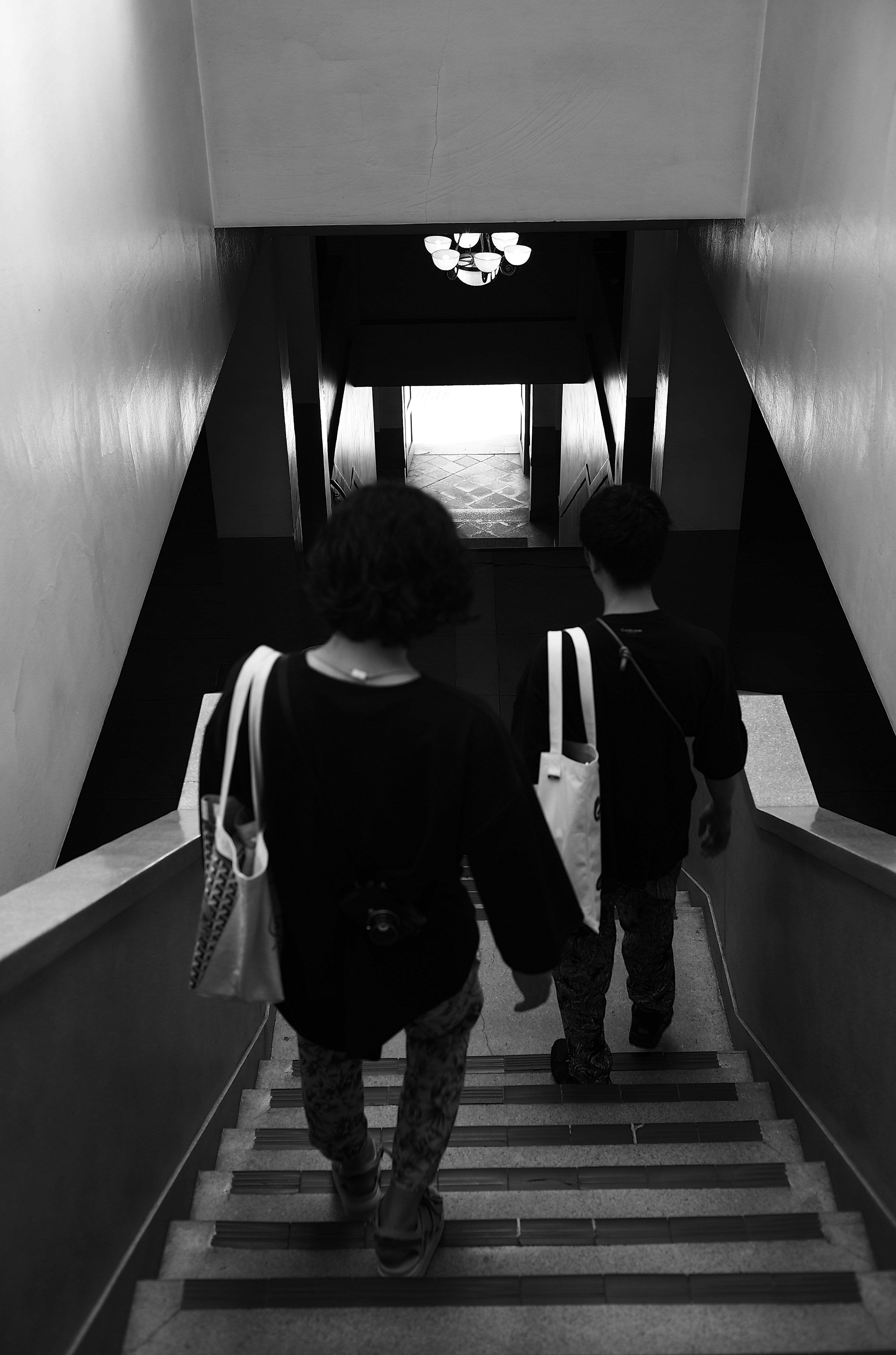 Two people walking down a staircase Black and white photo Bright exit visible