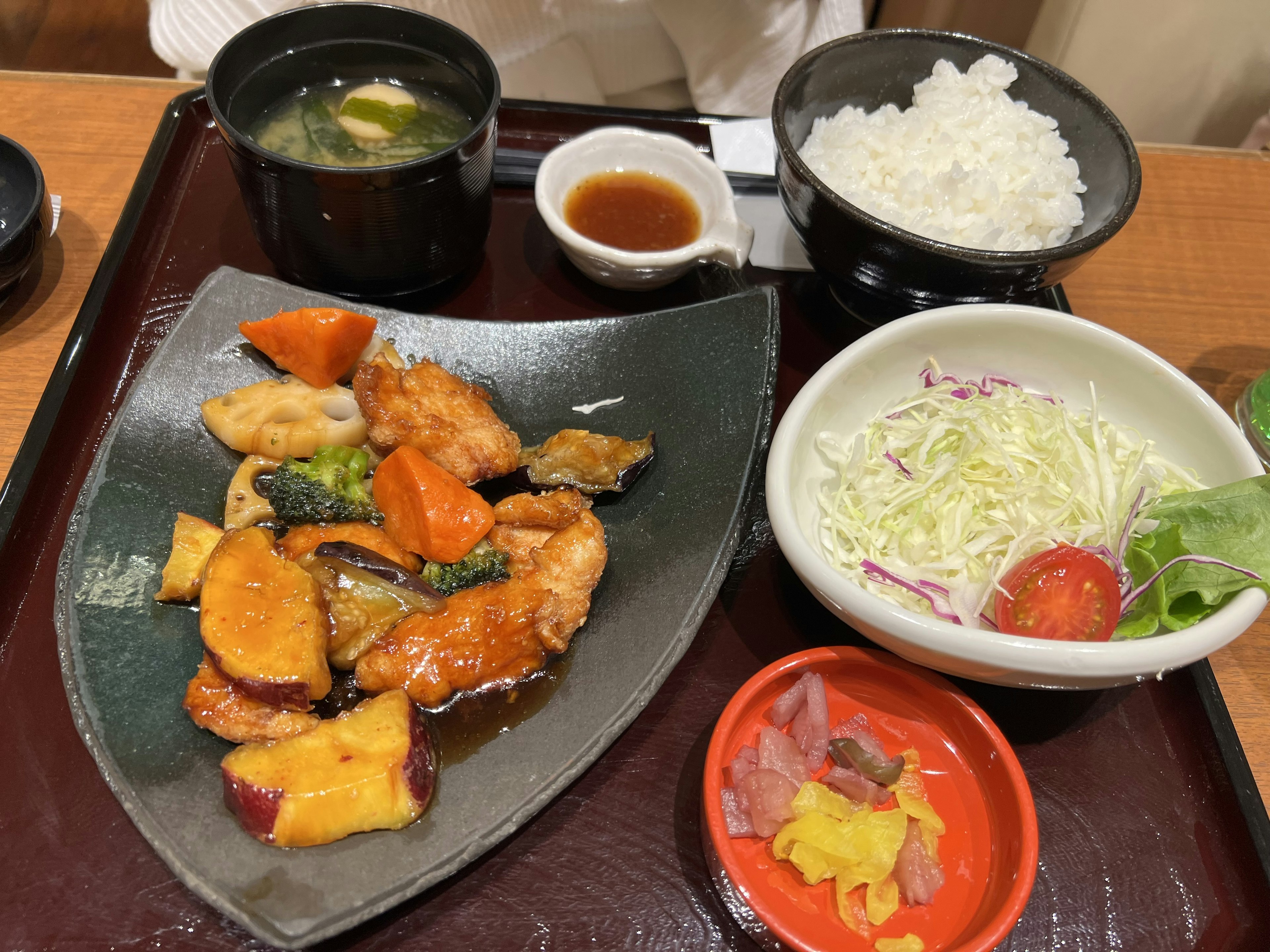 色とりどりの野菜と鶏肉の料理、ライス、味噌汁、サラダ、ソースが添えられた和食のプレート