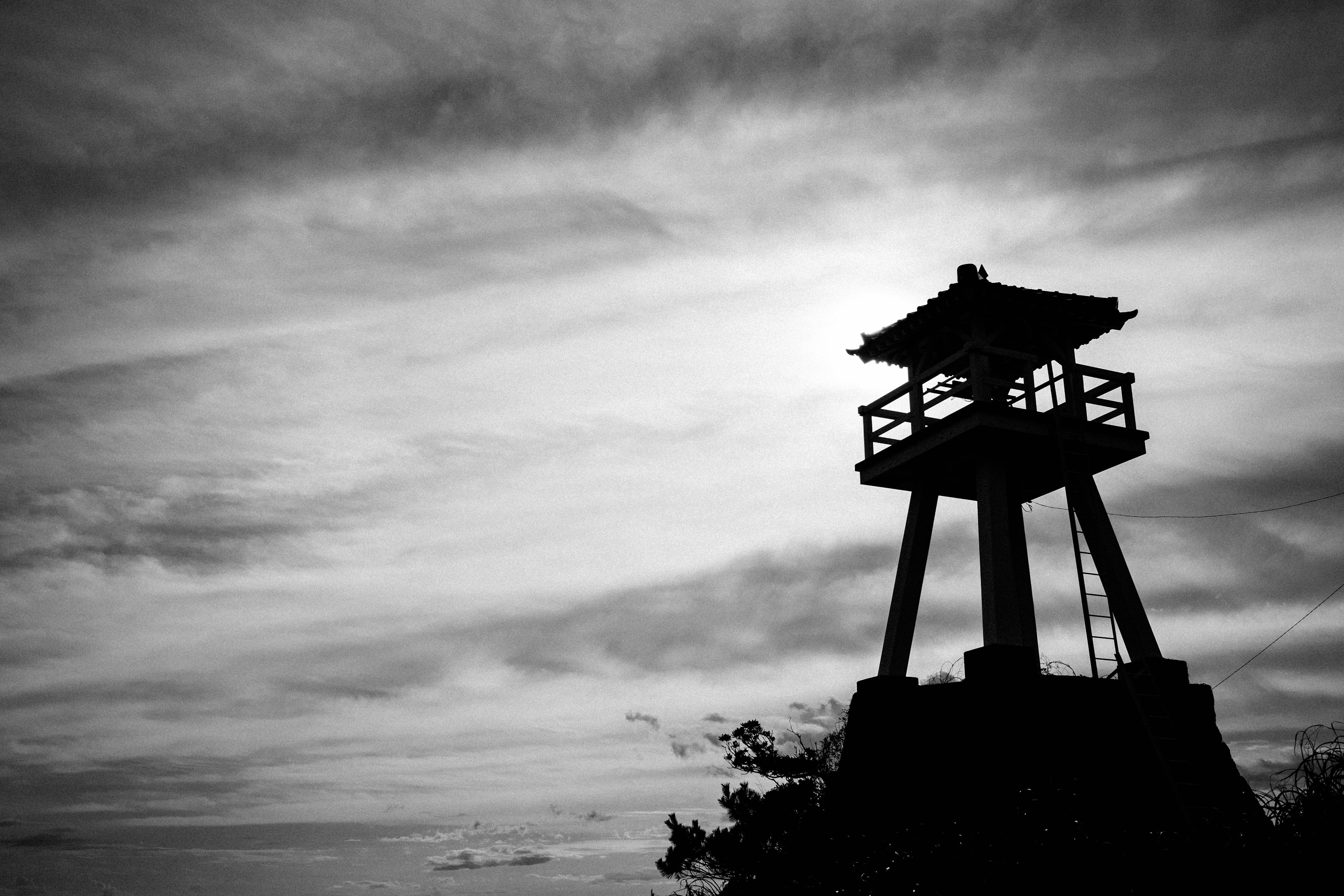 Silhouette di una torre di avvistamento contro un cielo nuvoloso in bianco e nero