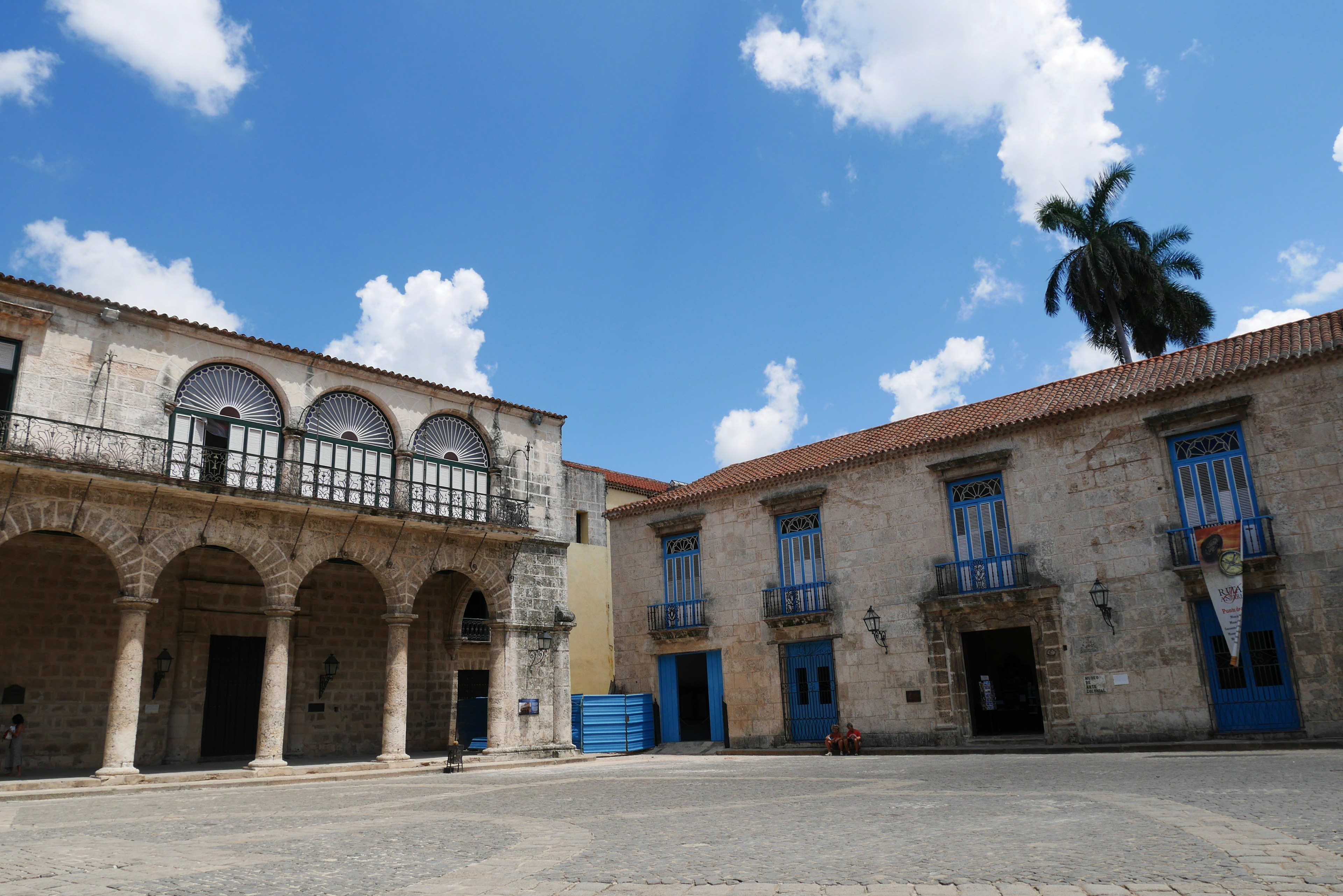 Square featuring old buildings and arched porch under a blue sky