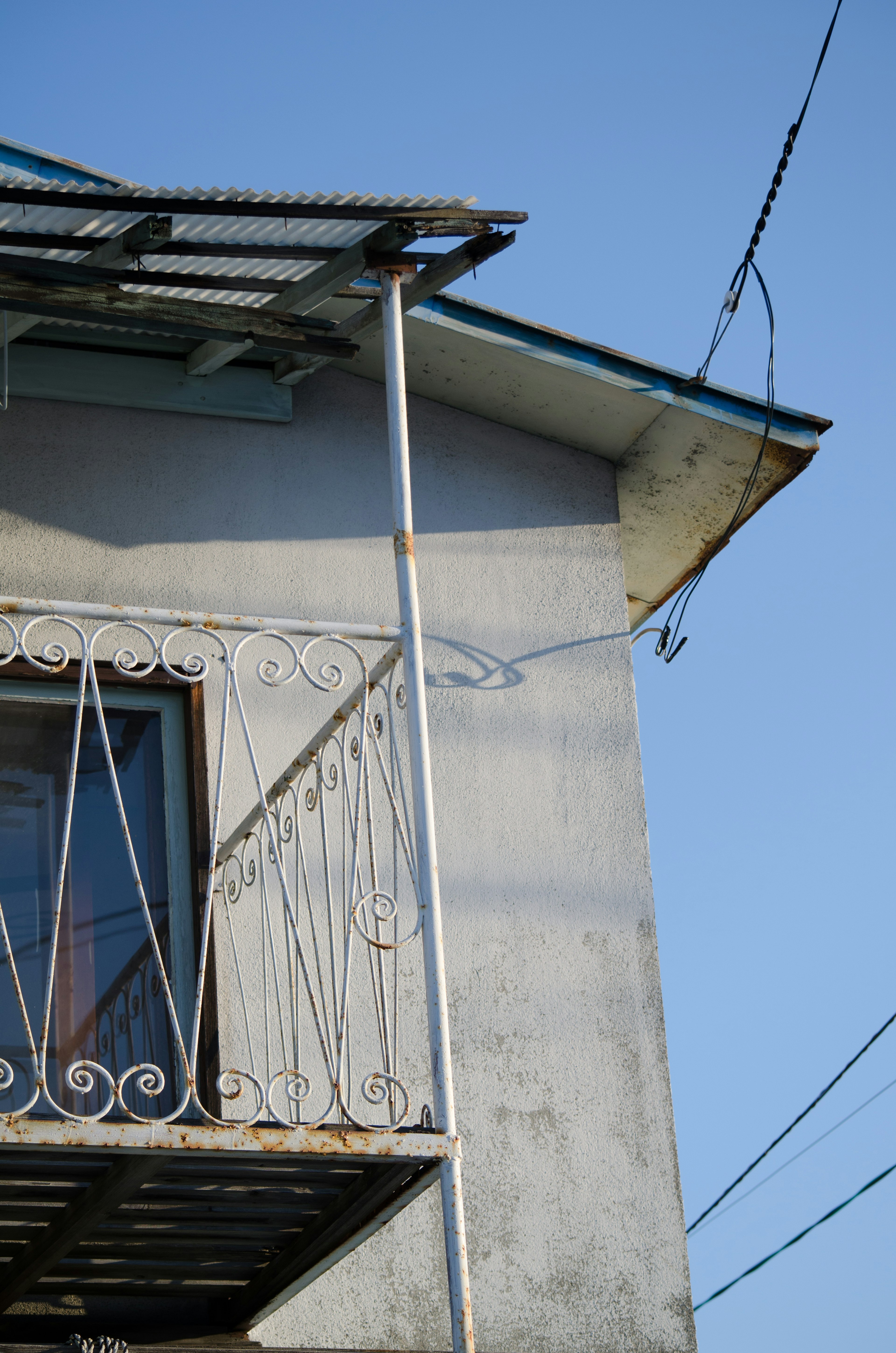 Section d'une vieille maison blanche sous un ciel bleu avec un garde-corps de balcon en métal