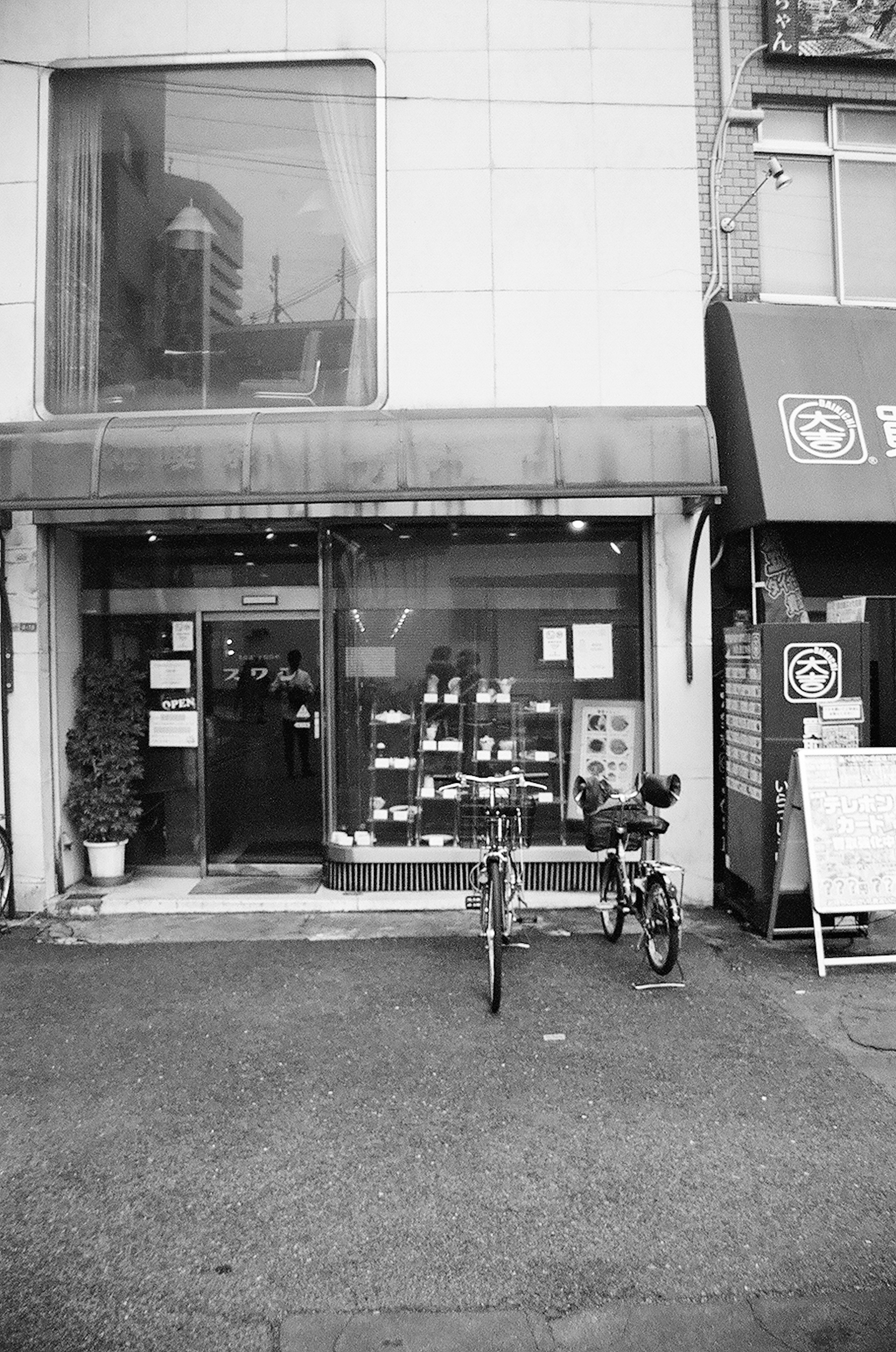 Foto en blanco y negro de una tienda con una bicicleta estacionada frente y productos exhibidos en la ventana