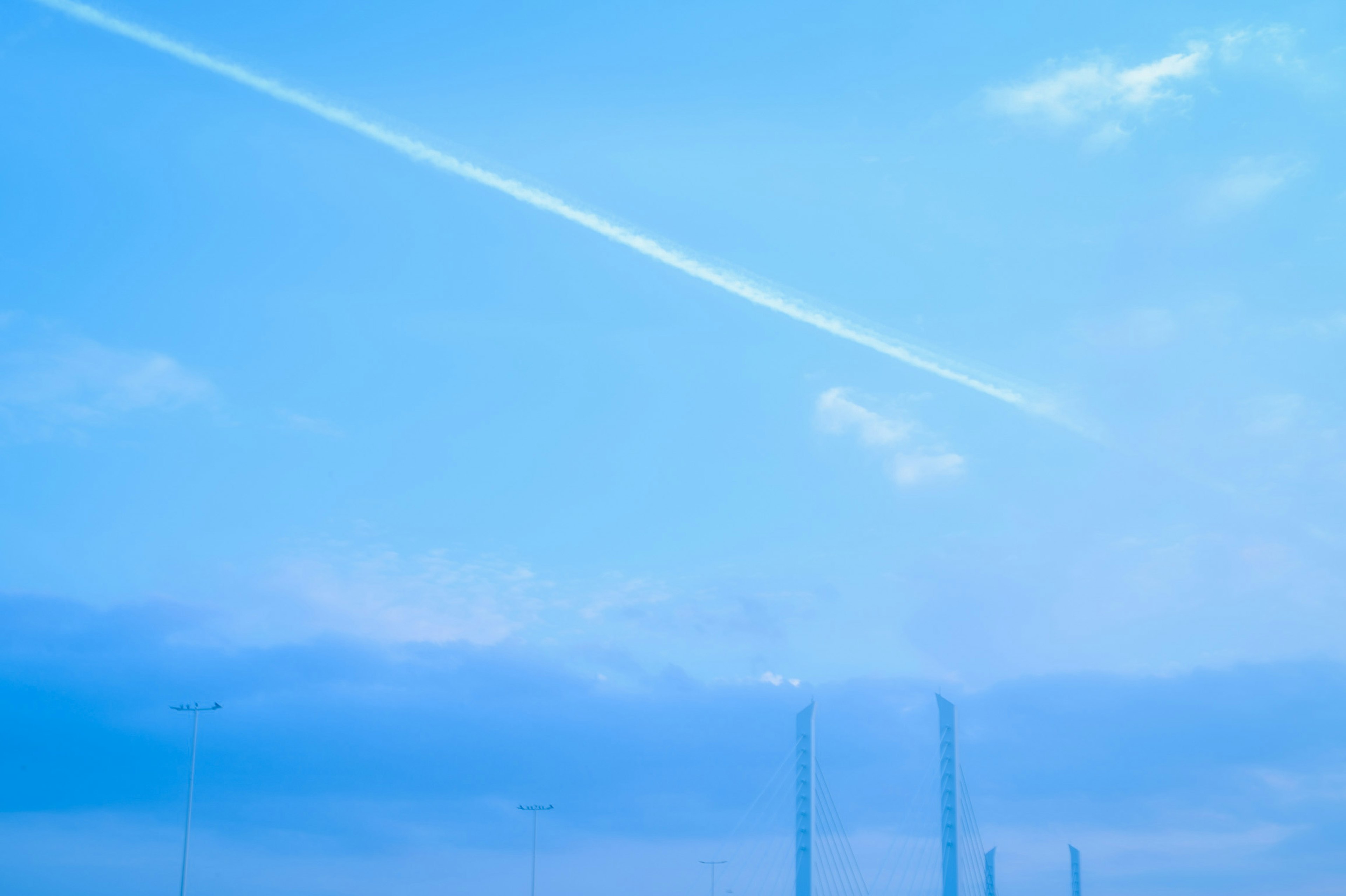 青空と雲が広がる風景に、飛行機雲と工場の煙突が見える