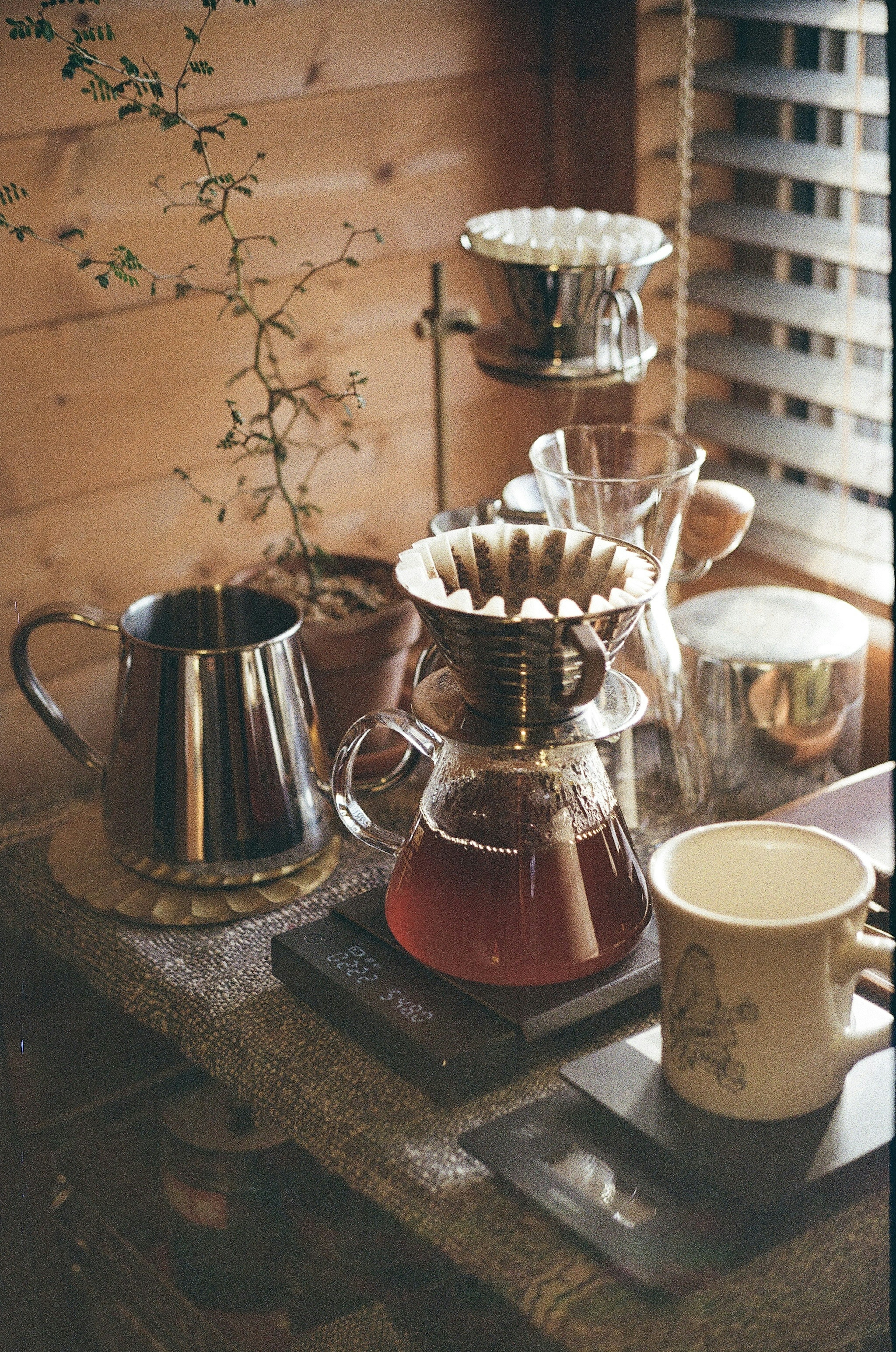 A wooden table displaying coffee brewing equipment with a kettle and mugs