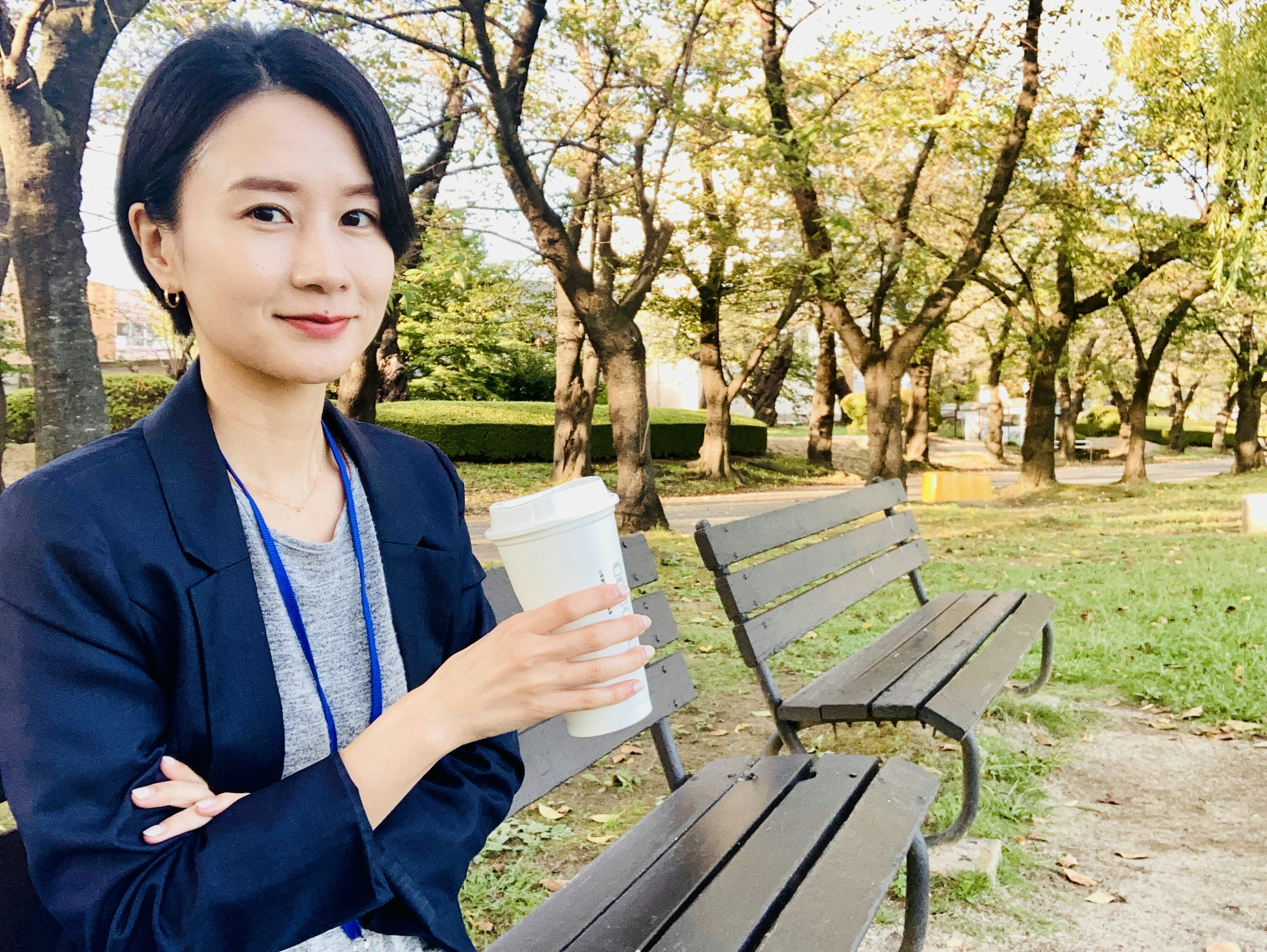 Une femme assise sur un banc de parc tenant une tasse de café et souriant