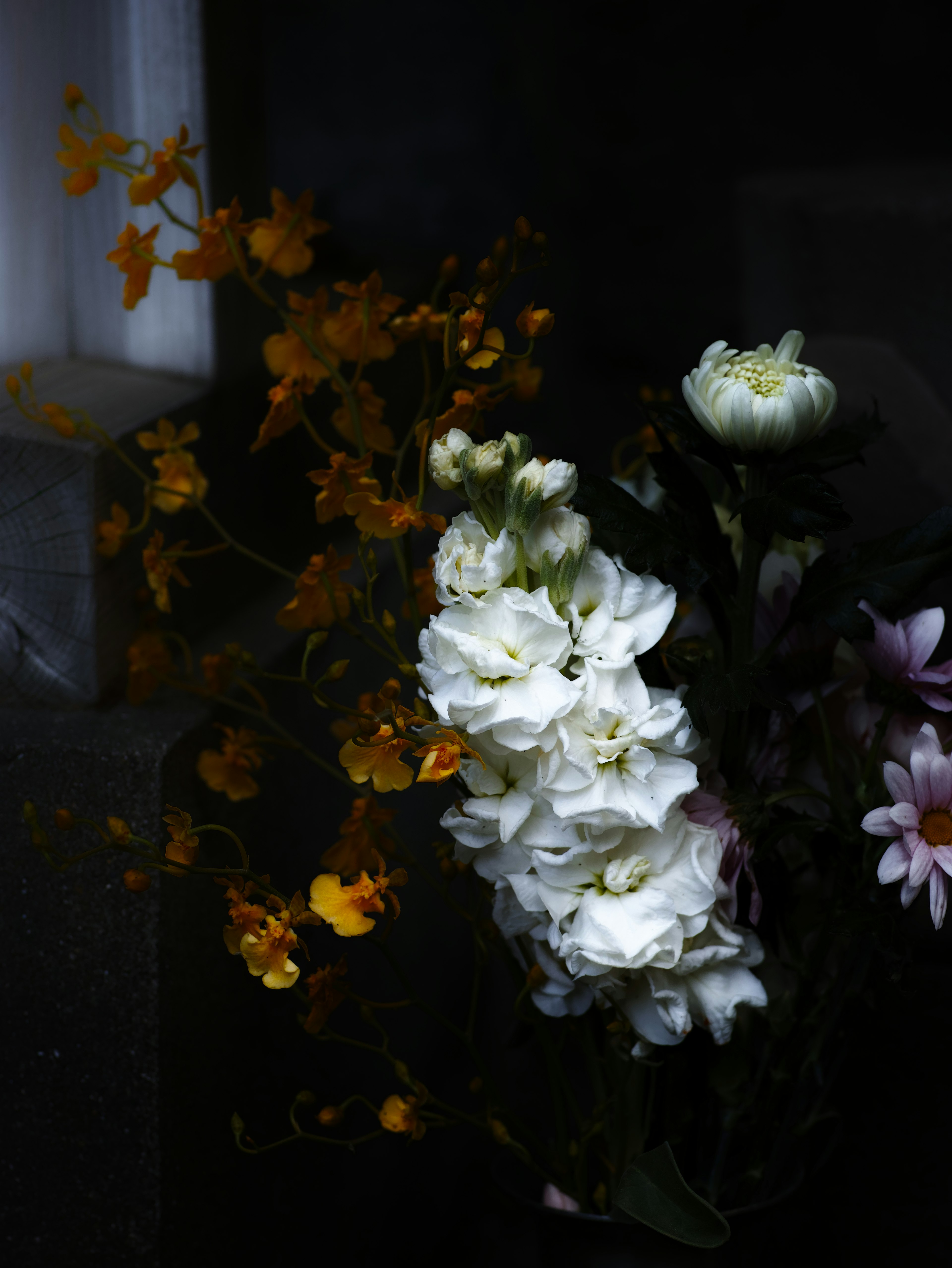 暗い背景に白い花と黄色い花が混ざった花束