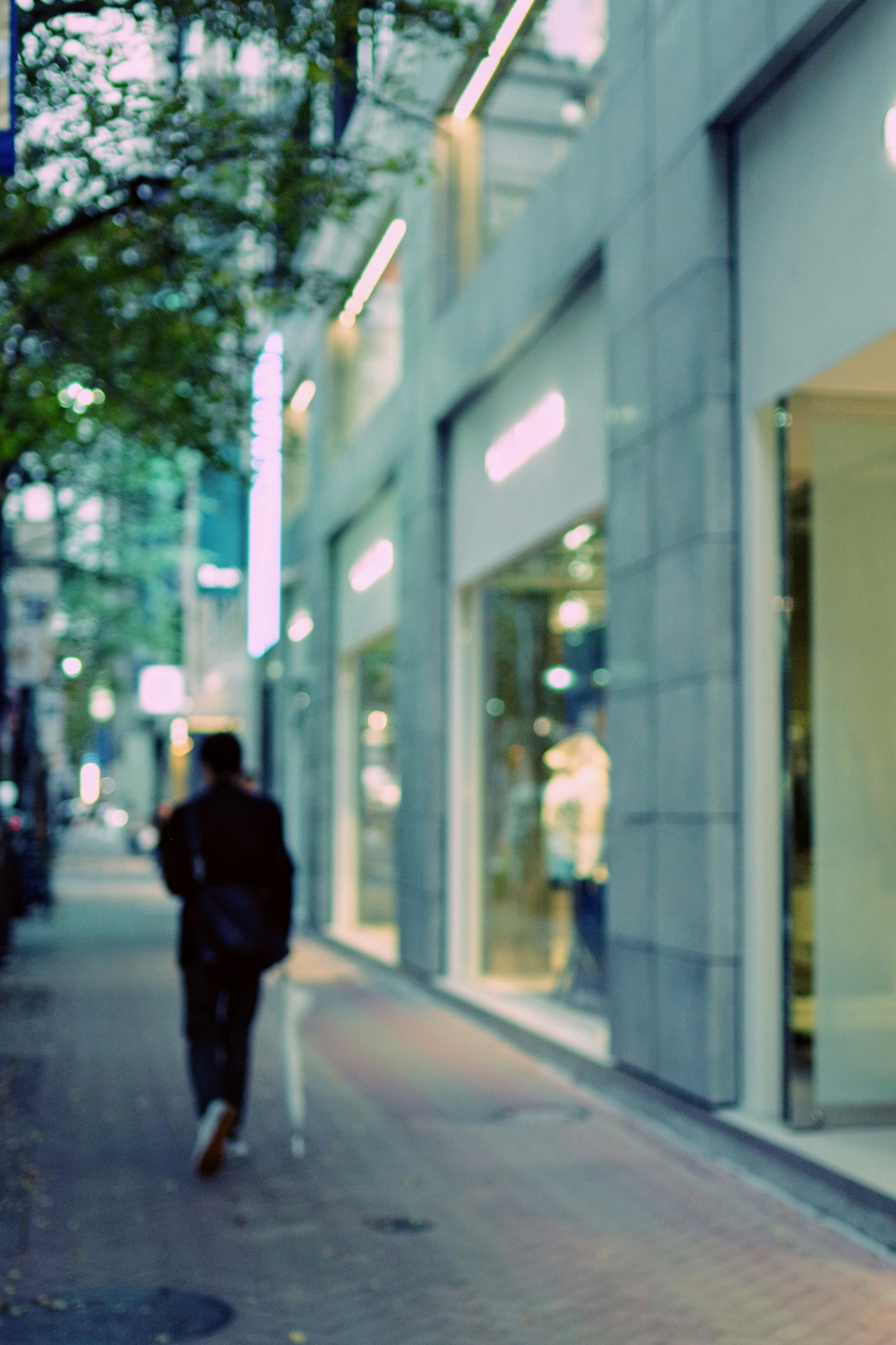 A blurred silhouette of a person walking down a street with shop windows