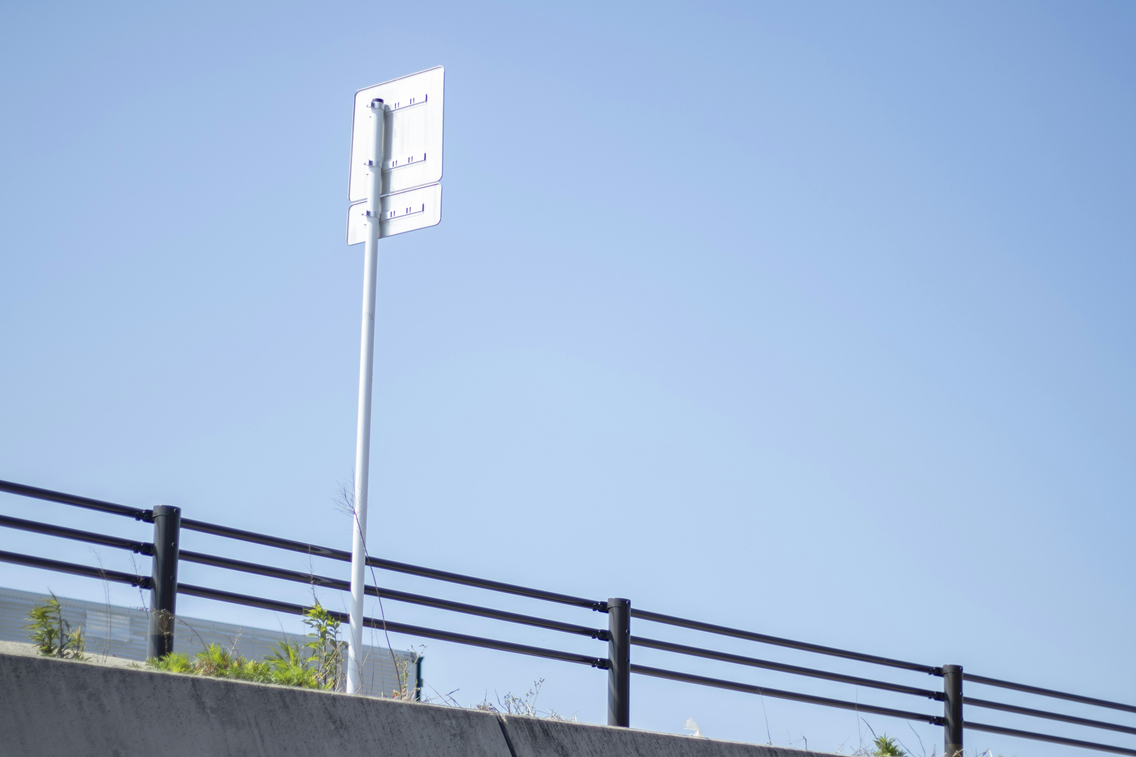 Ein weißes Verkehrsschild vor einem blauen Himmel mit einem Metallzaun