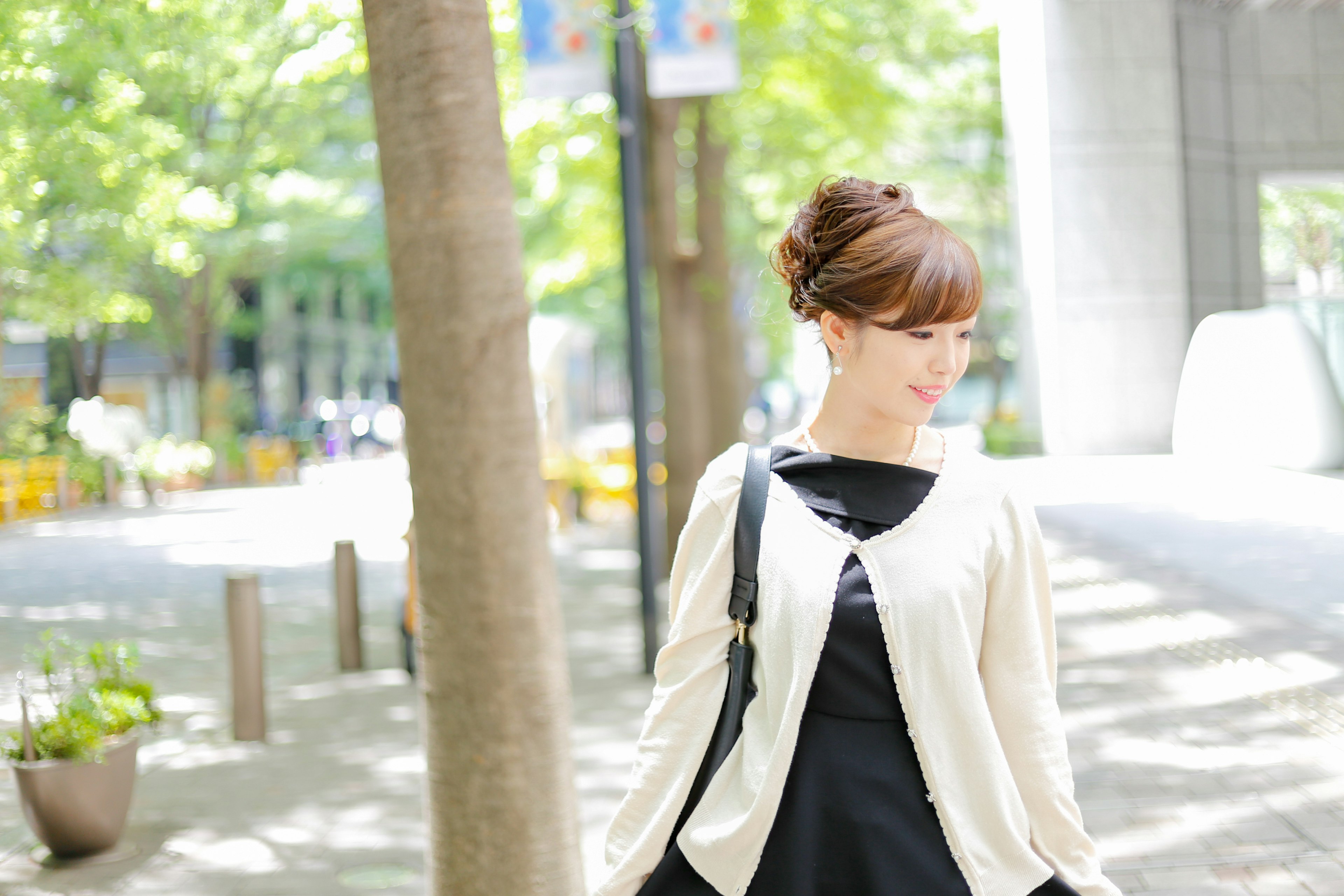 Femme portant une robe noire et un cardigan blanc marchant dans un cadre urbain