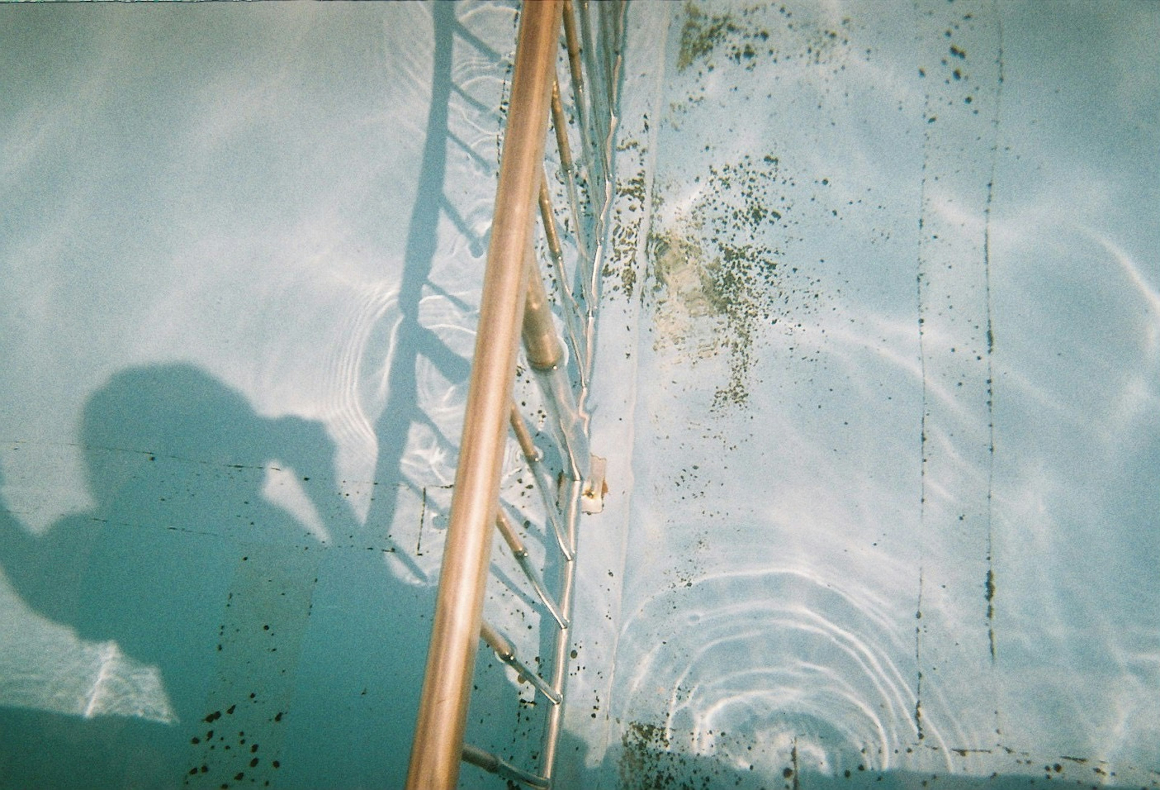 Escalera reflejada en el agua con sombra y superficie azul de la piscina