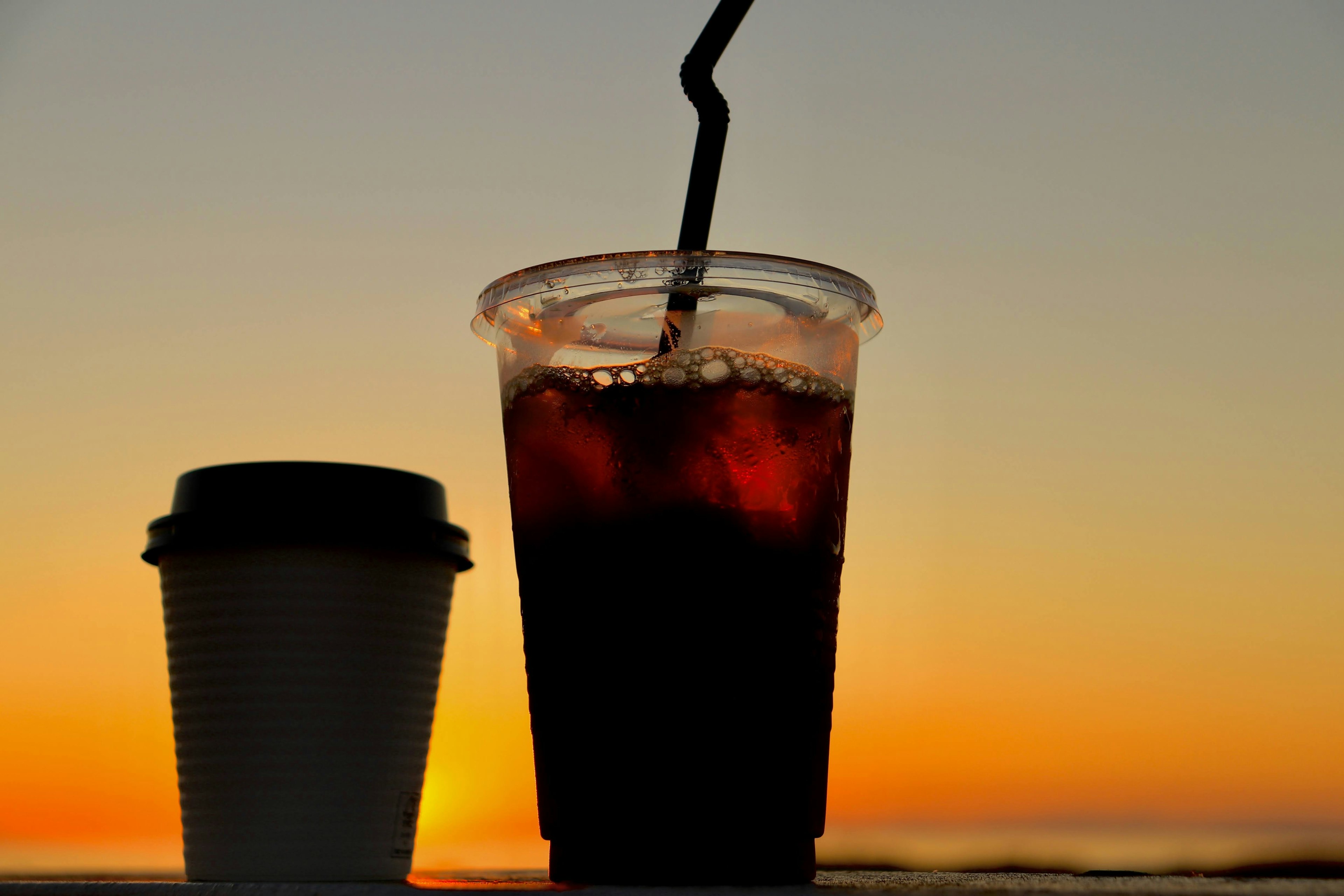 Silueta de una taza de café y una bebida helada contra un atardecer