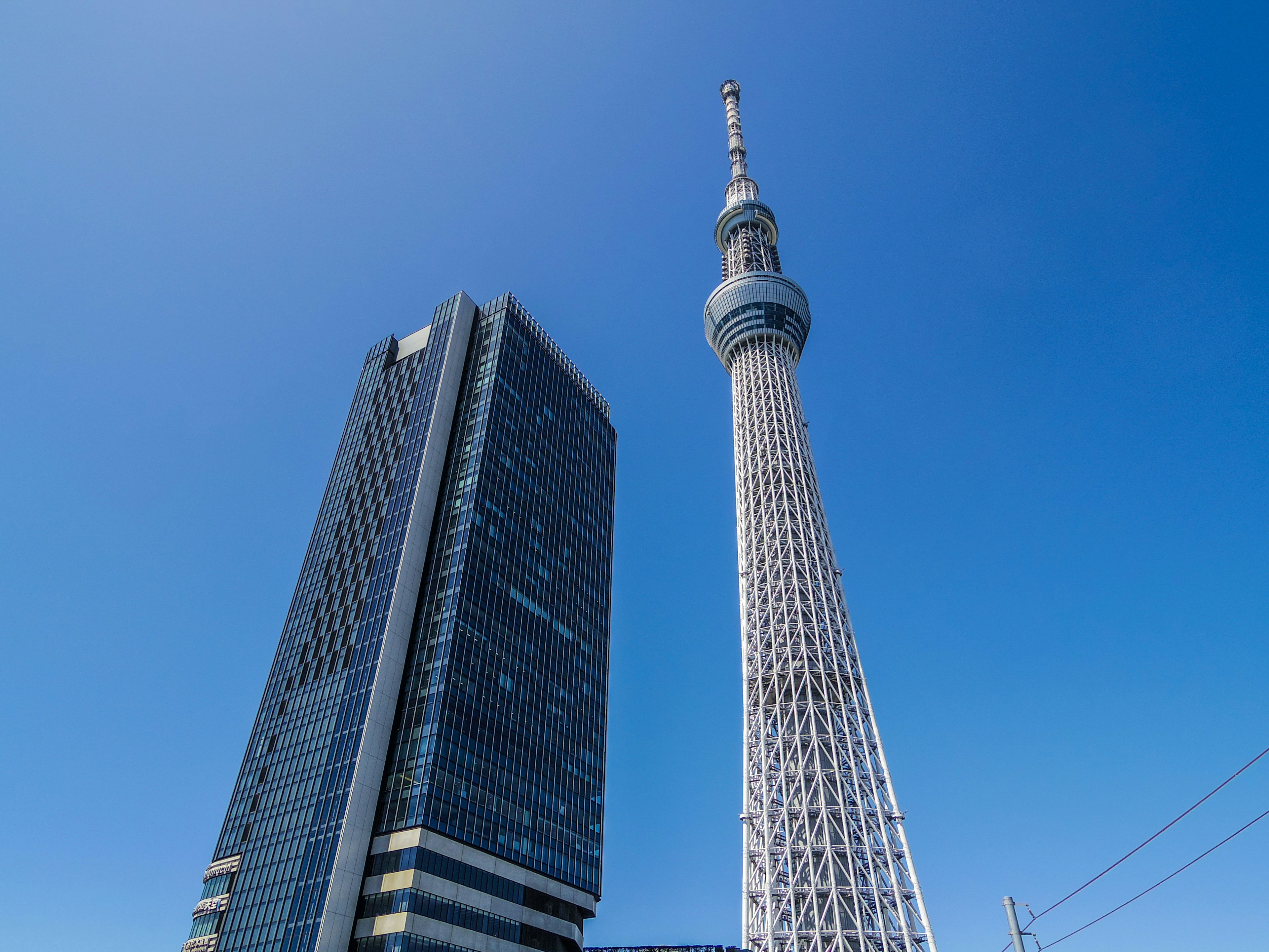 Tokyo Skytree bên cạnh một tòa nhà chọc trời hiện đại dưới bầu trời xanh rõ ràng