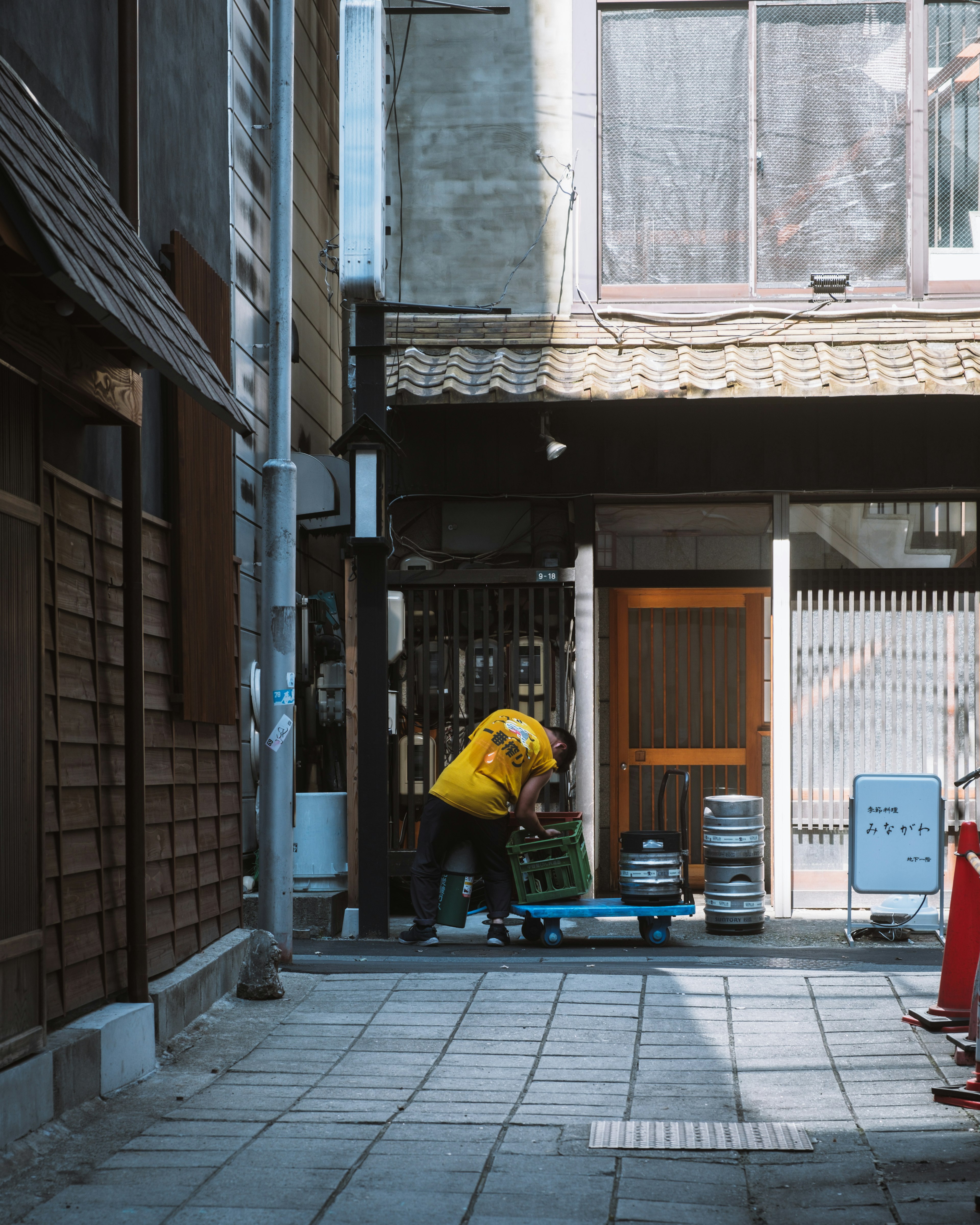 A worker in a yellow shirt is working in a narrow alley