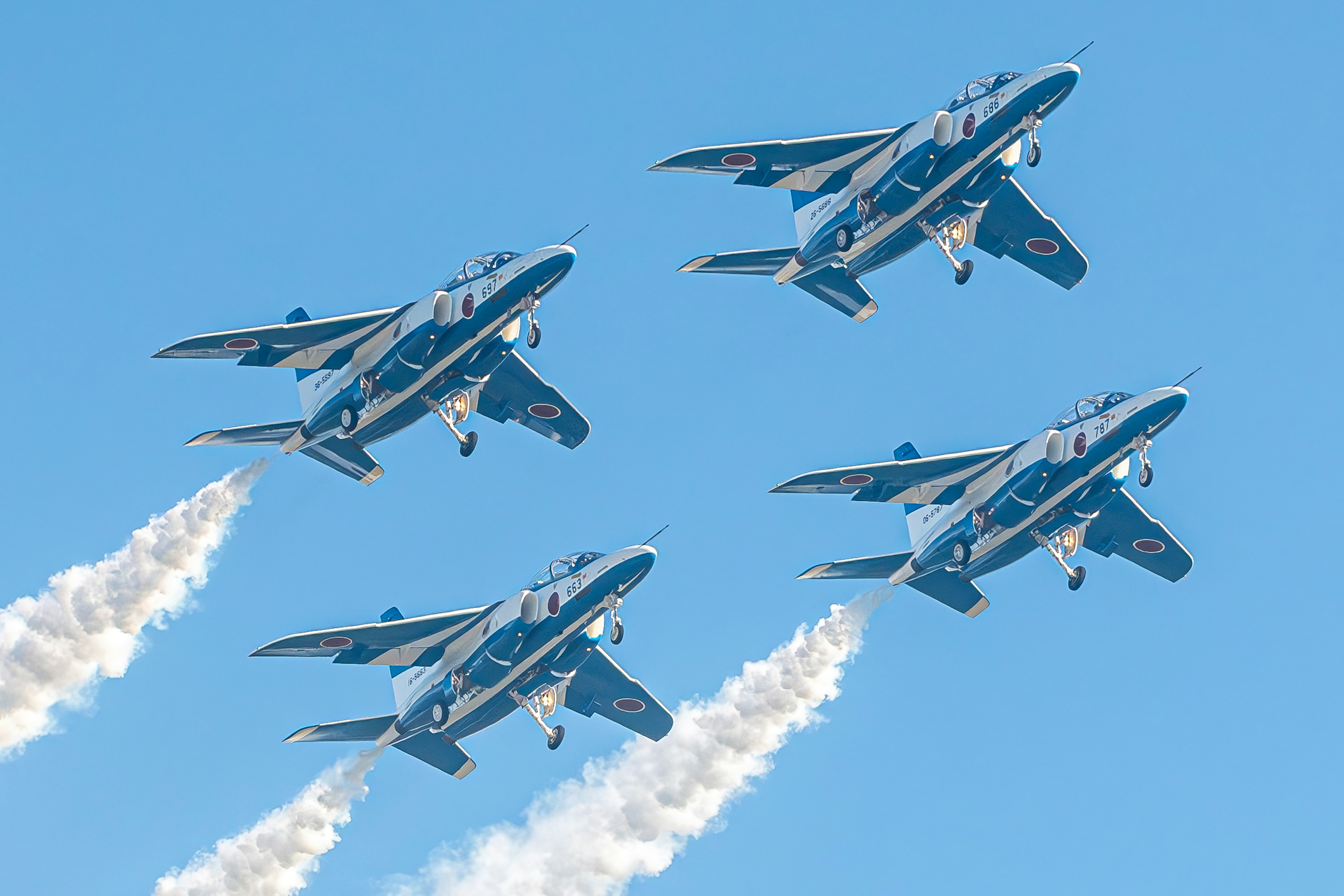 青い機体の4機の戦闘機が煙を吐きながら飛行している