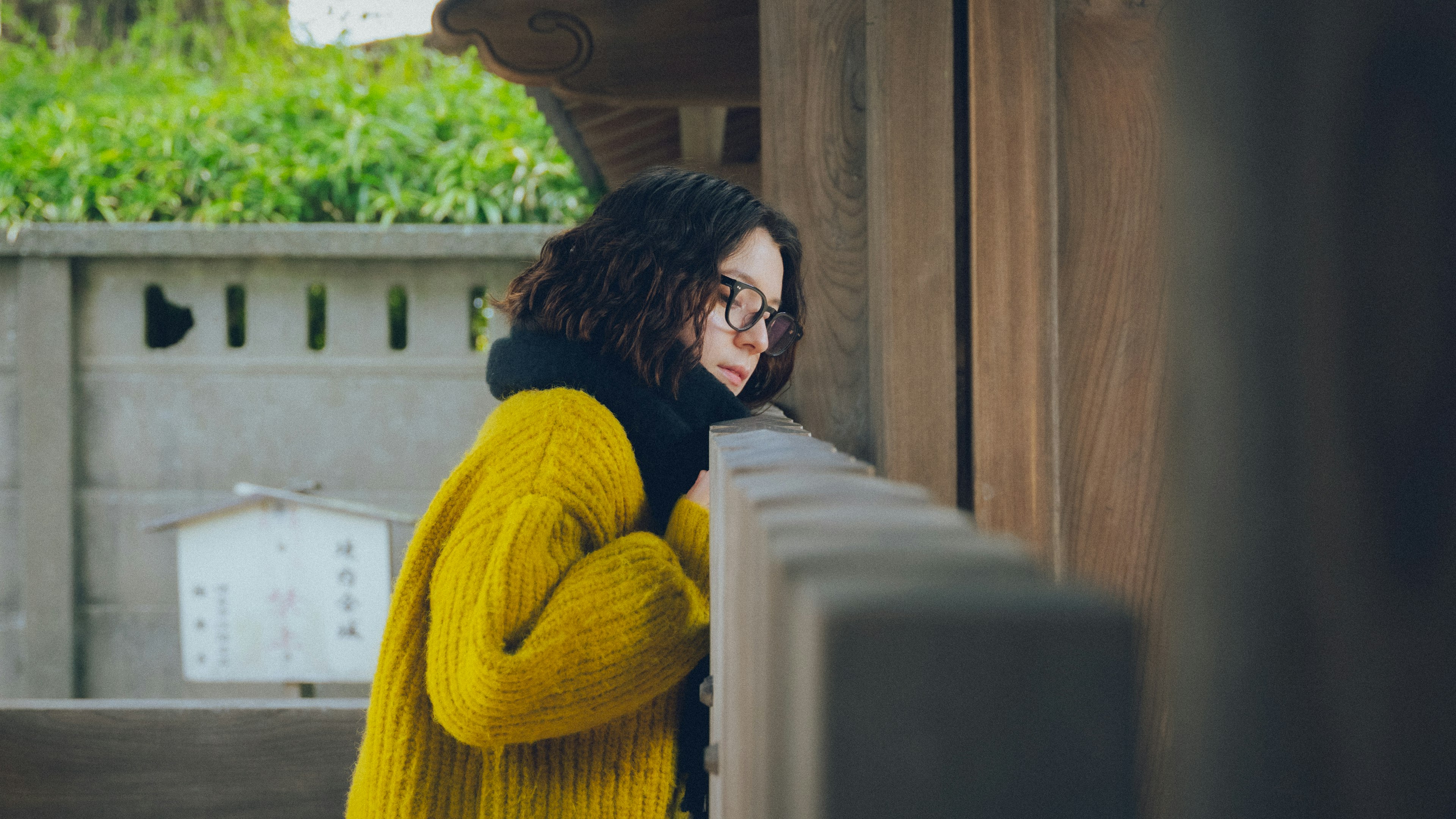 明るい黄色のセーターを着た女性が木のフェンスに寄りかかっている