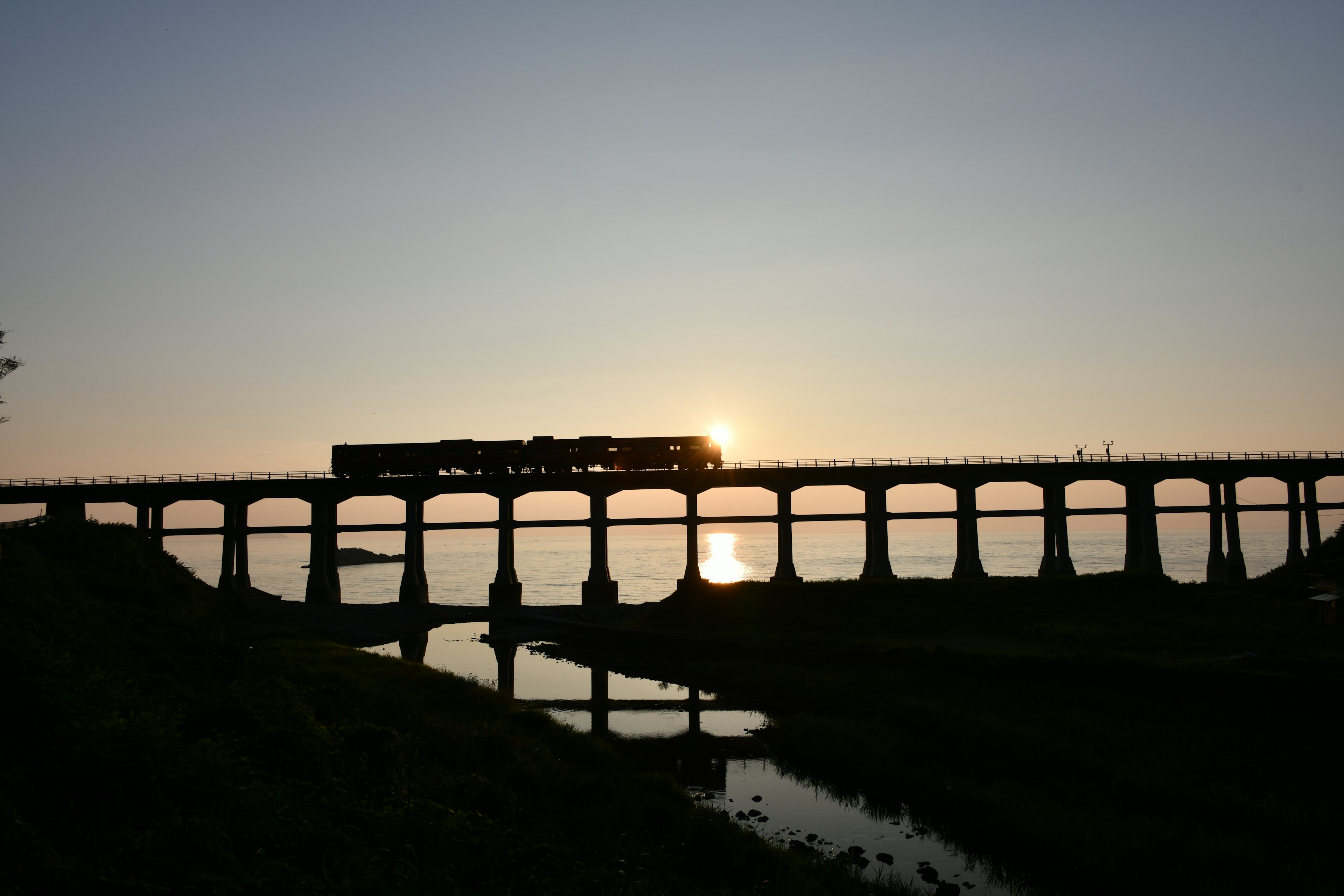 Silhouette eines Zuges, der eine Eisenbahnbrücke bei Sonnenuntergang überquert