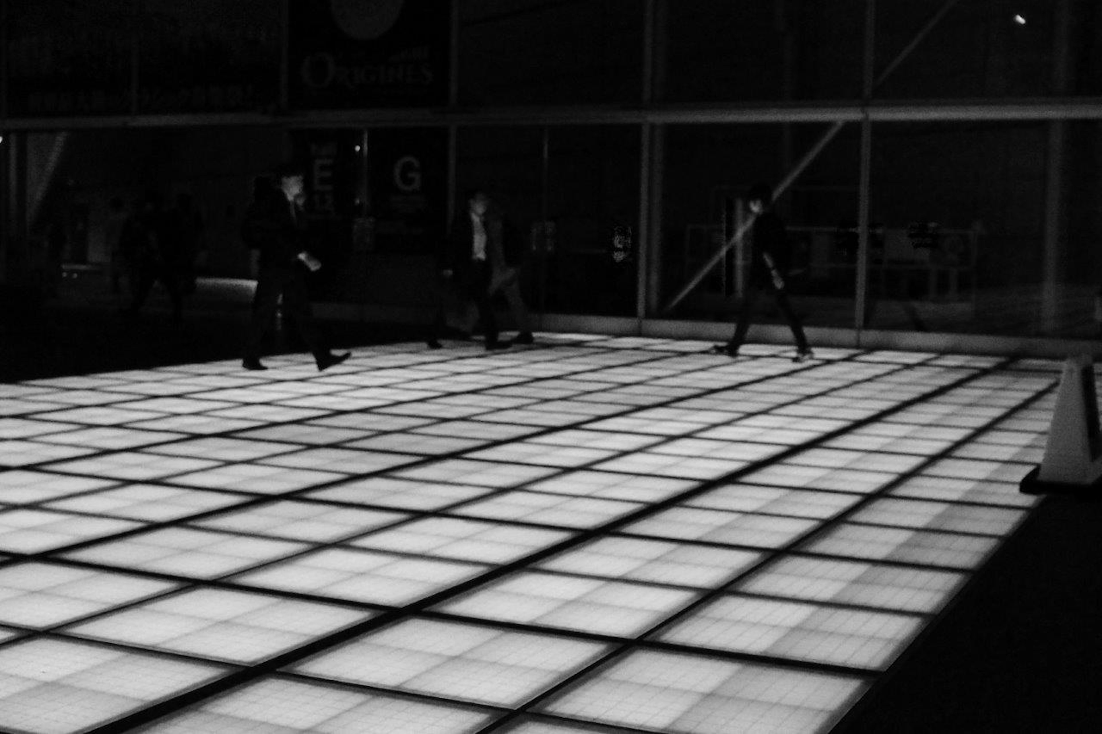 People walking on a glowing tile floor in a dark setting