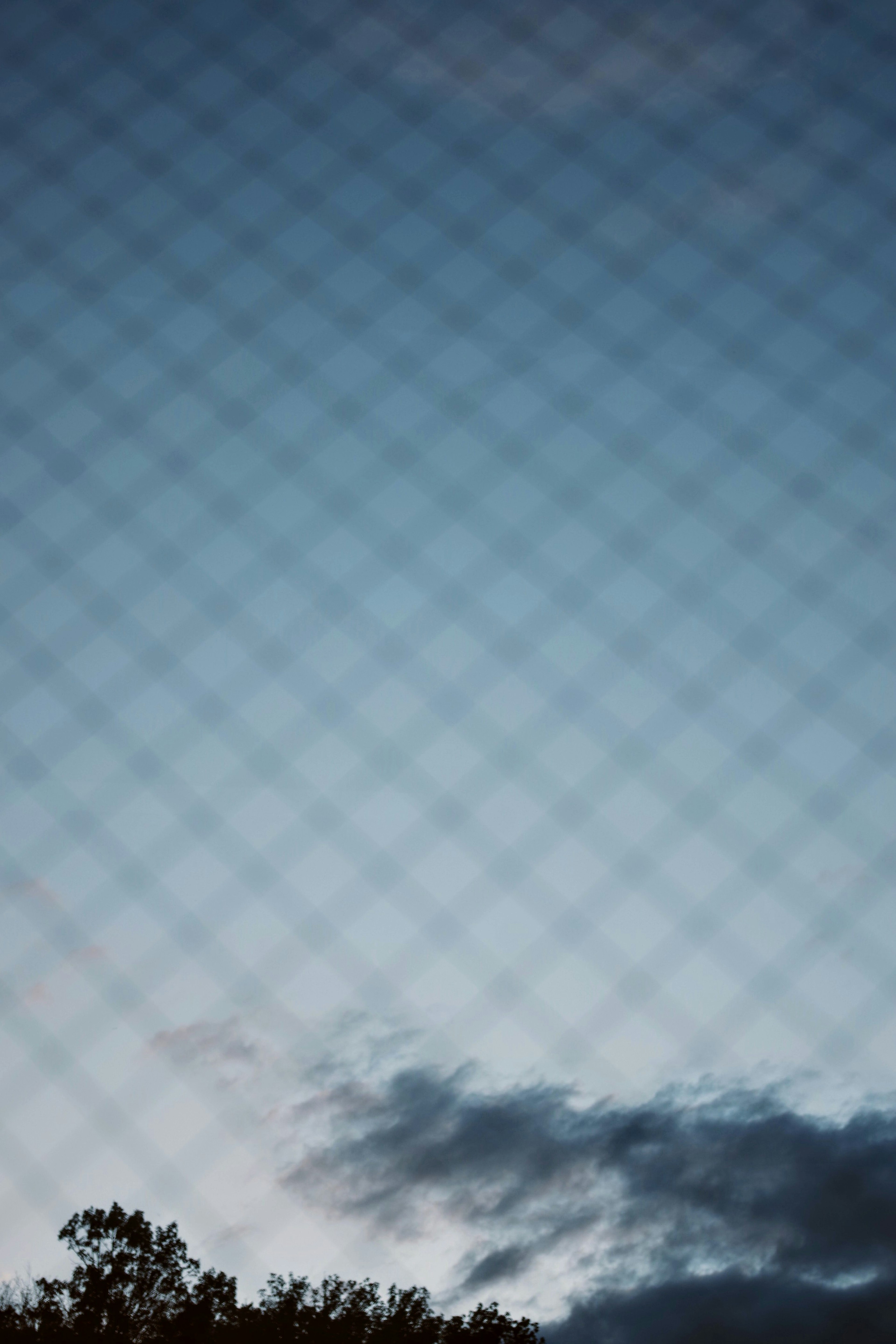 View of blue sky and cloud silhouettes through a mesh fence