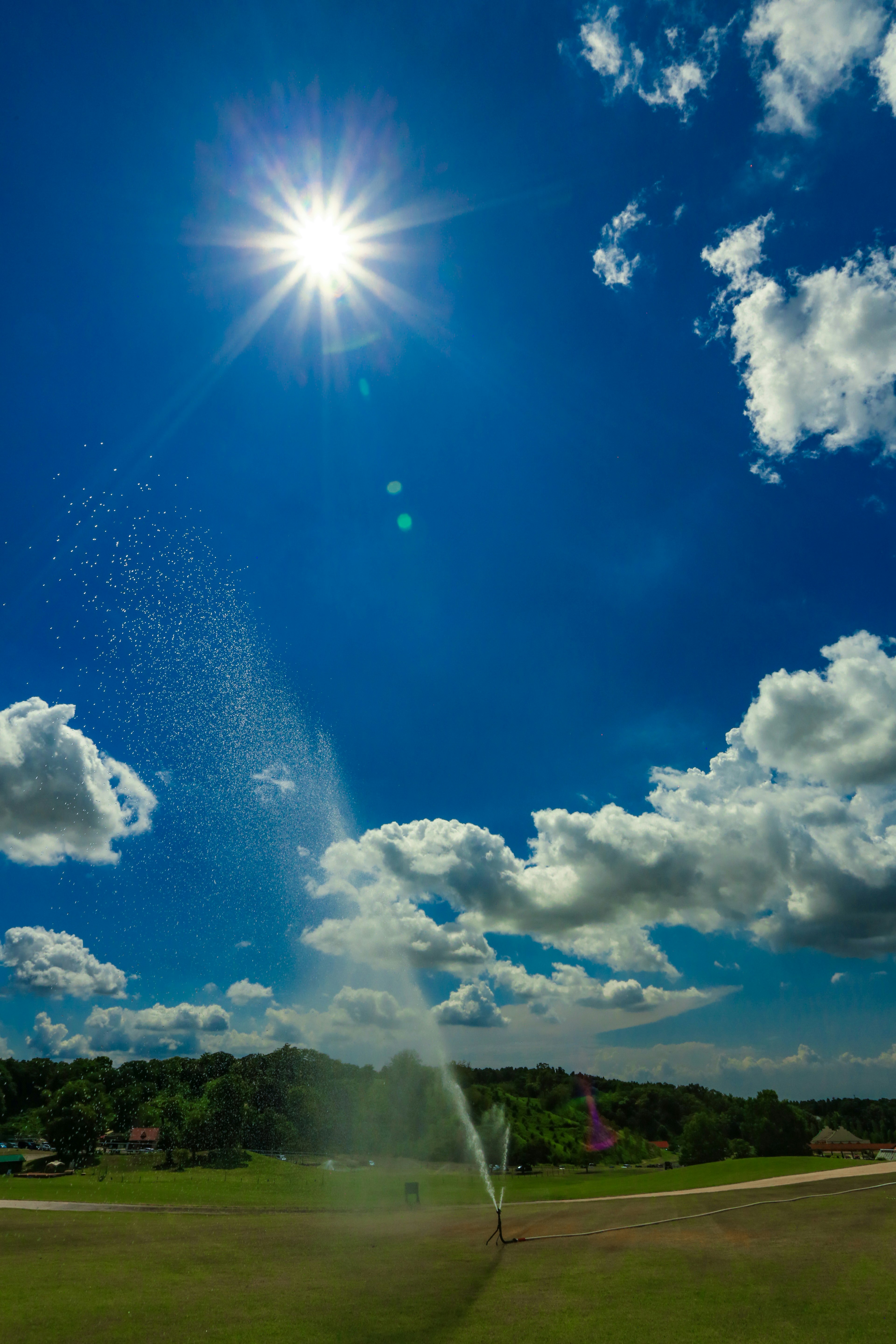 青空と白い雲の下で噴水が水を噴き上げている風景