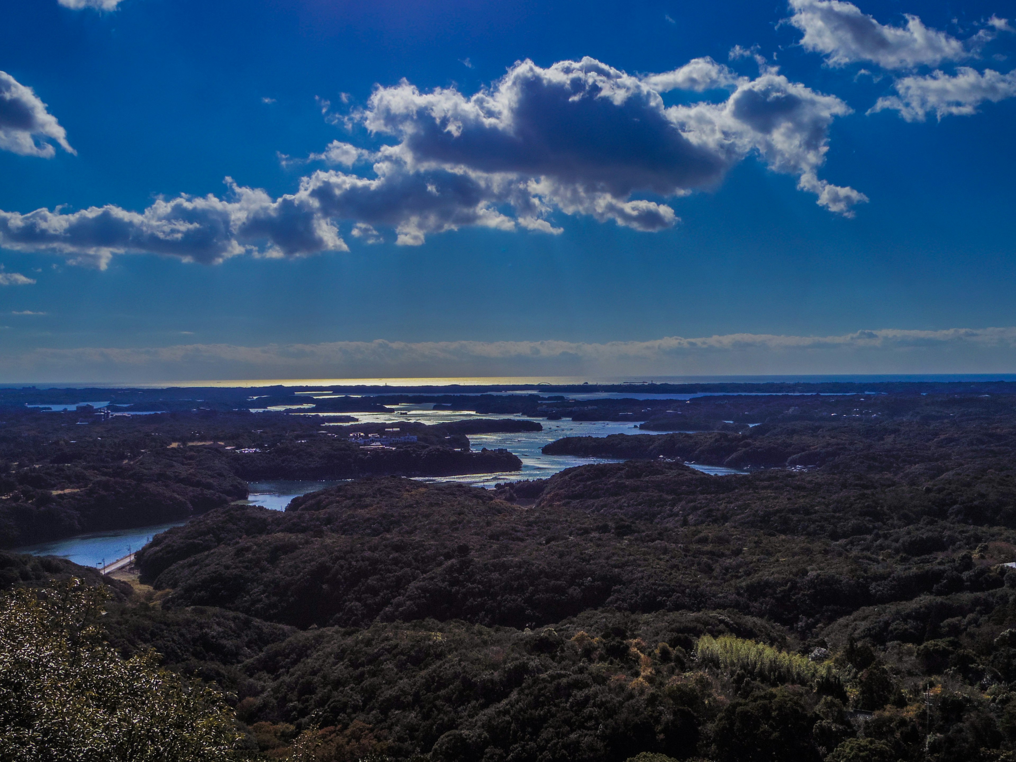 Ampia vista su un lago e una foresta sotto un cielo blu con nuvole