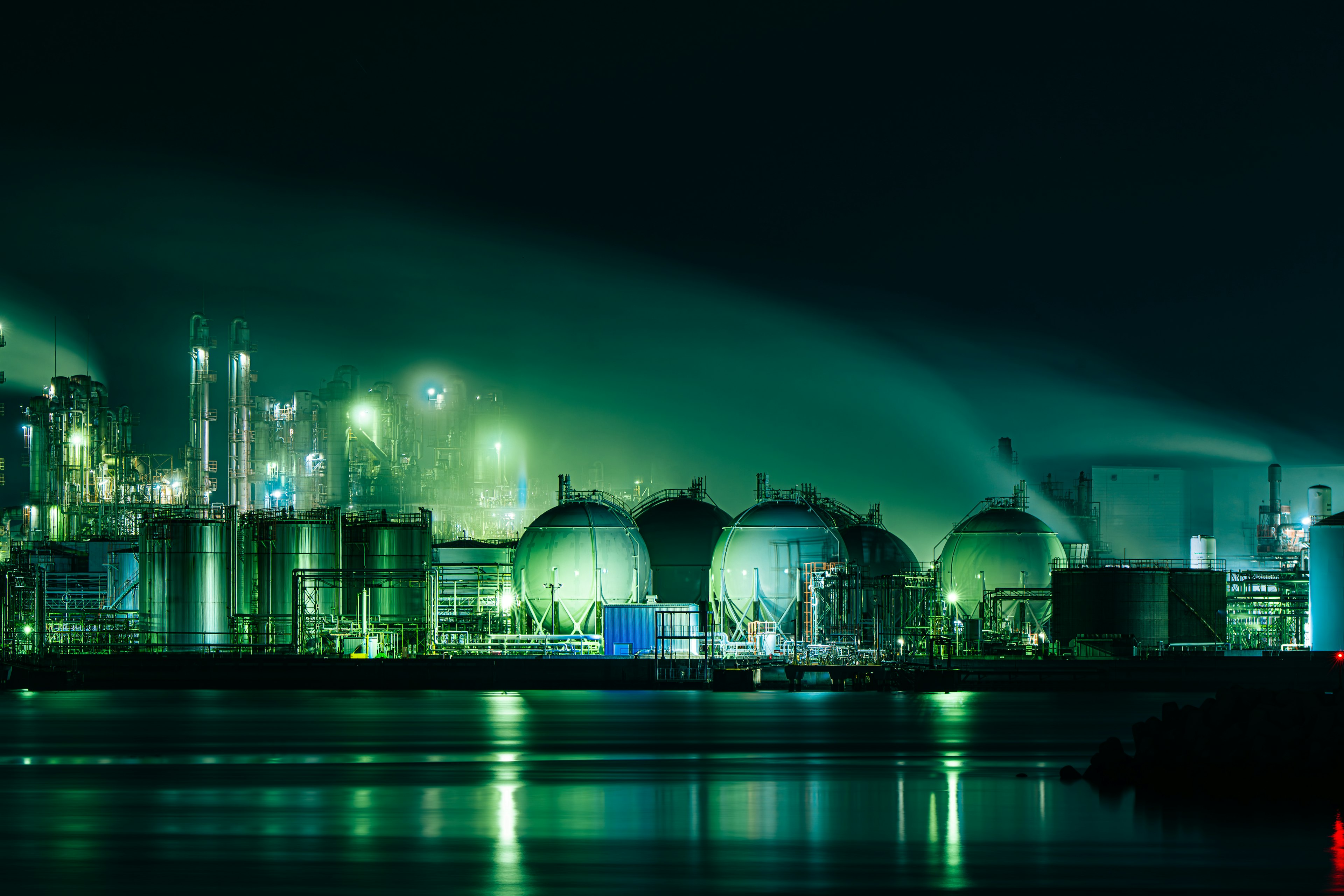 Industrial area at night featuring green tanks and smoke