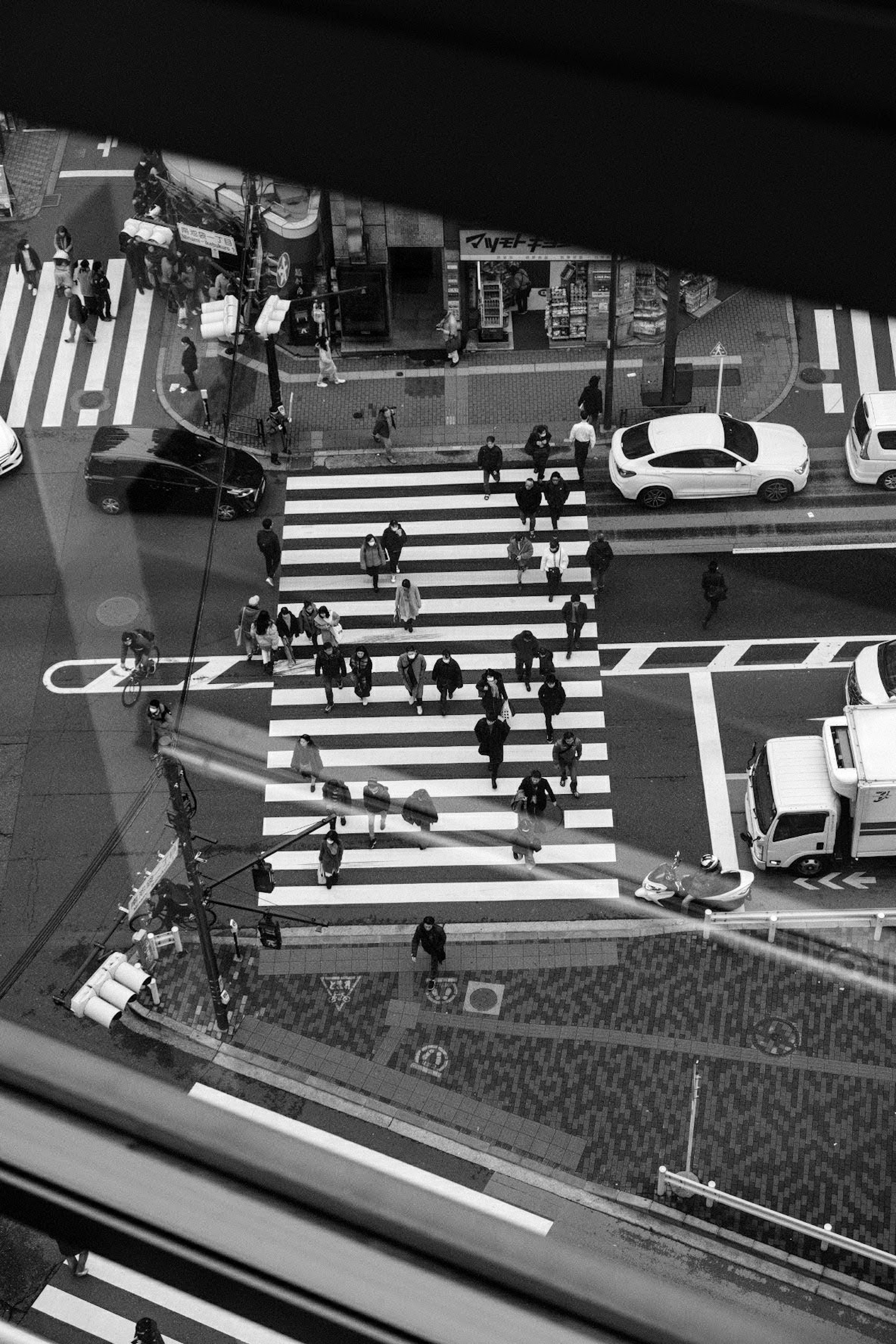 Aerial view of a busy crosswalk with numerous pedestrians and vehicles in black and white