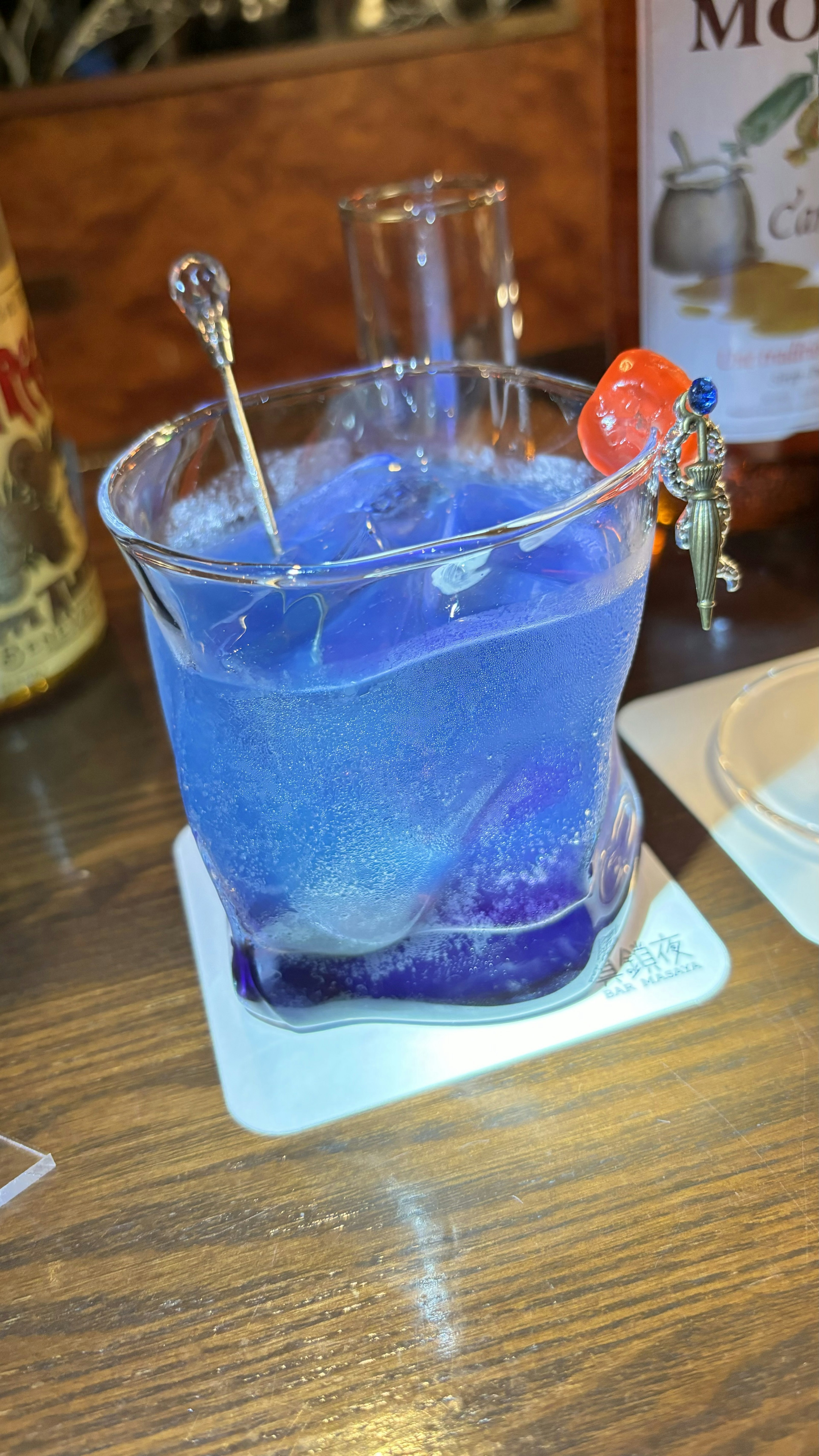 A blue drink in a laboratory glass with skewers and a cherry garnish