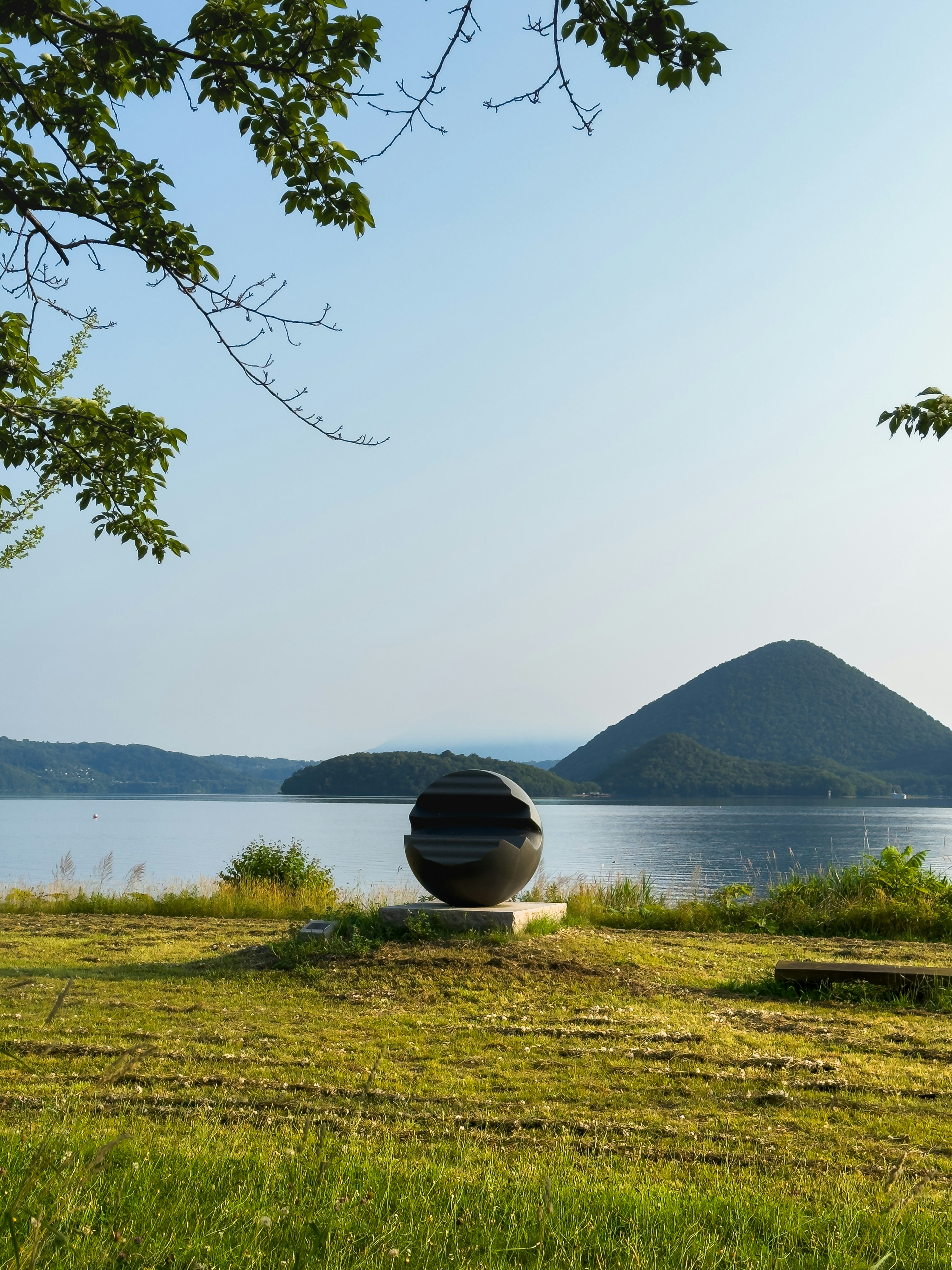 Black sculpture near a lake with a mountain in the background