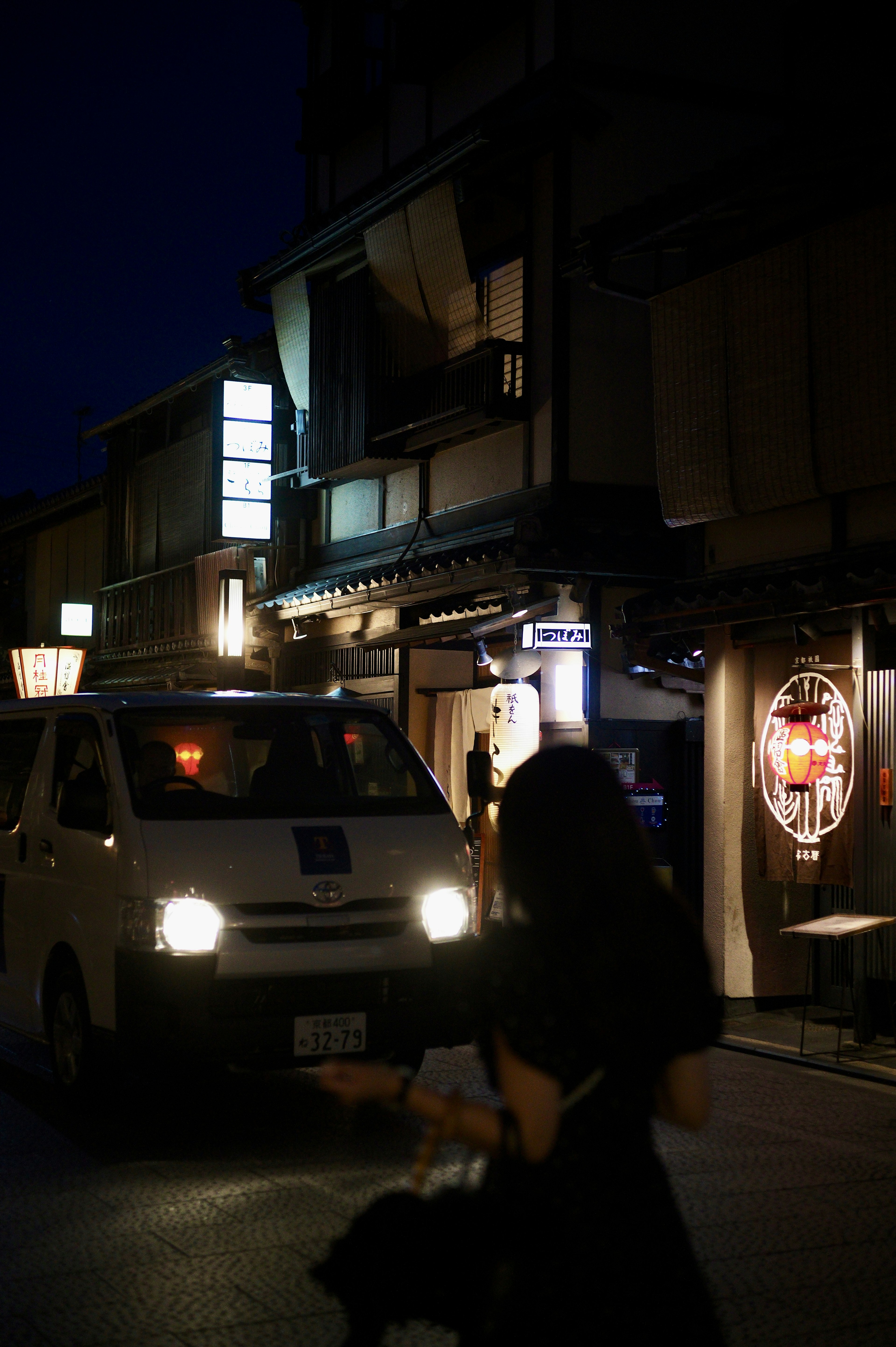 A woman walking in a city street at night with a passing van