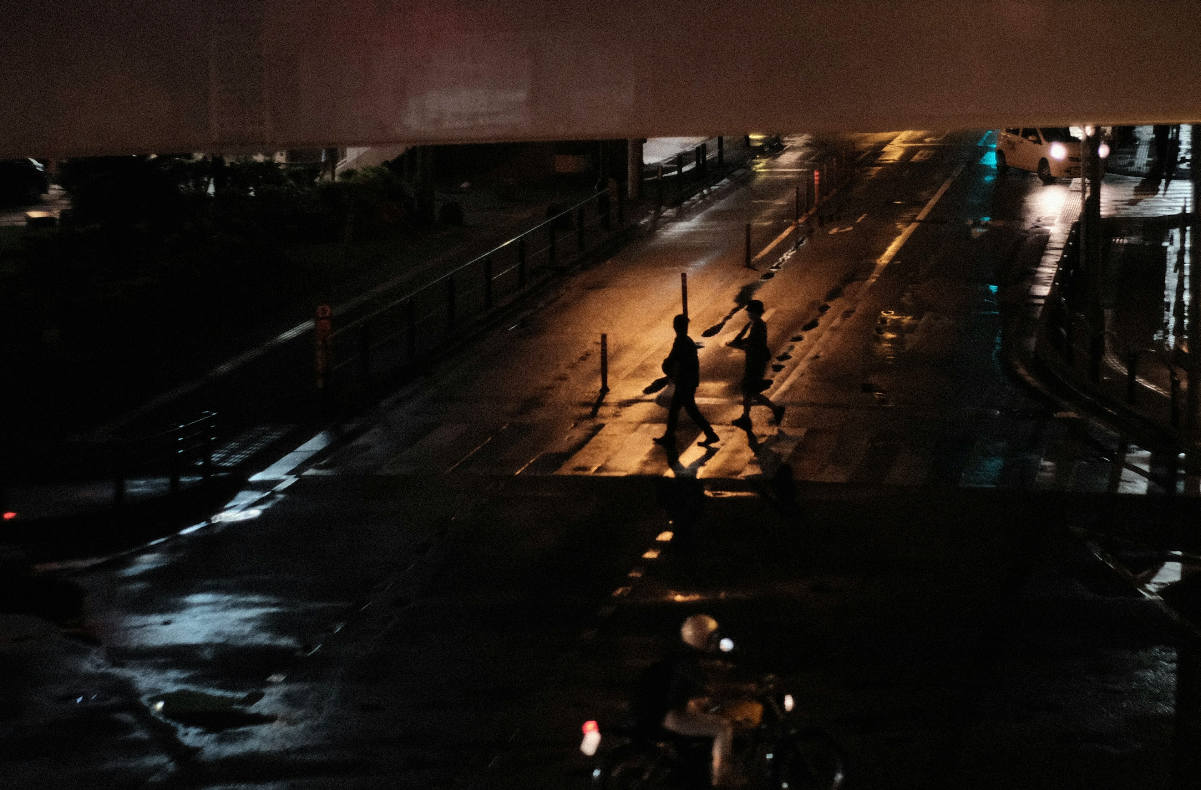 Silhouetten von Menschen, die nachts auf einer nassen Straße gehen