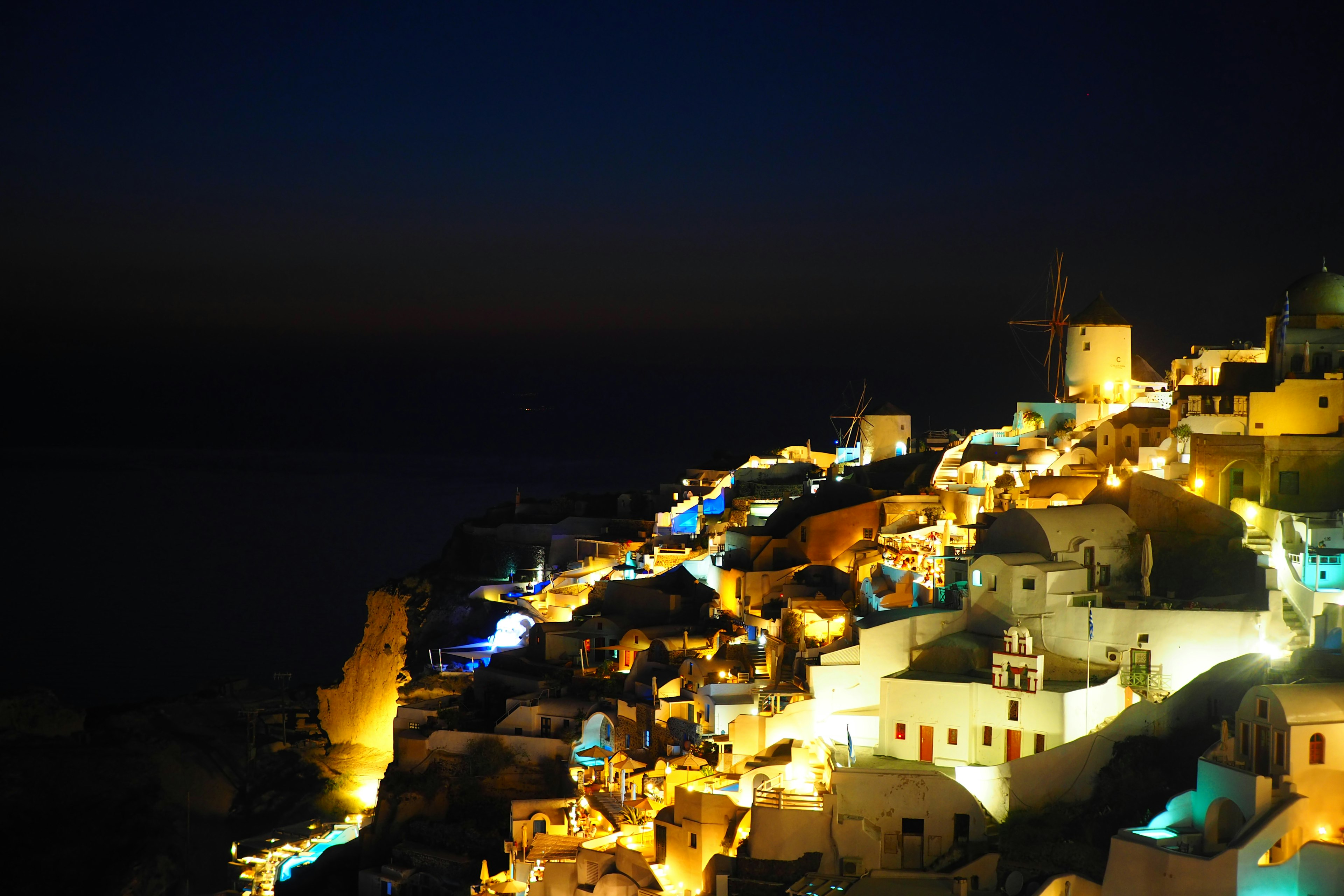 Wunderschöner Nachtblick auf die Insel Santorin mit hell erleuchteten weißen Gebäuden und einer Windmühle