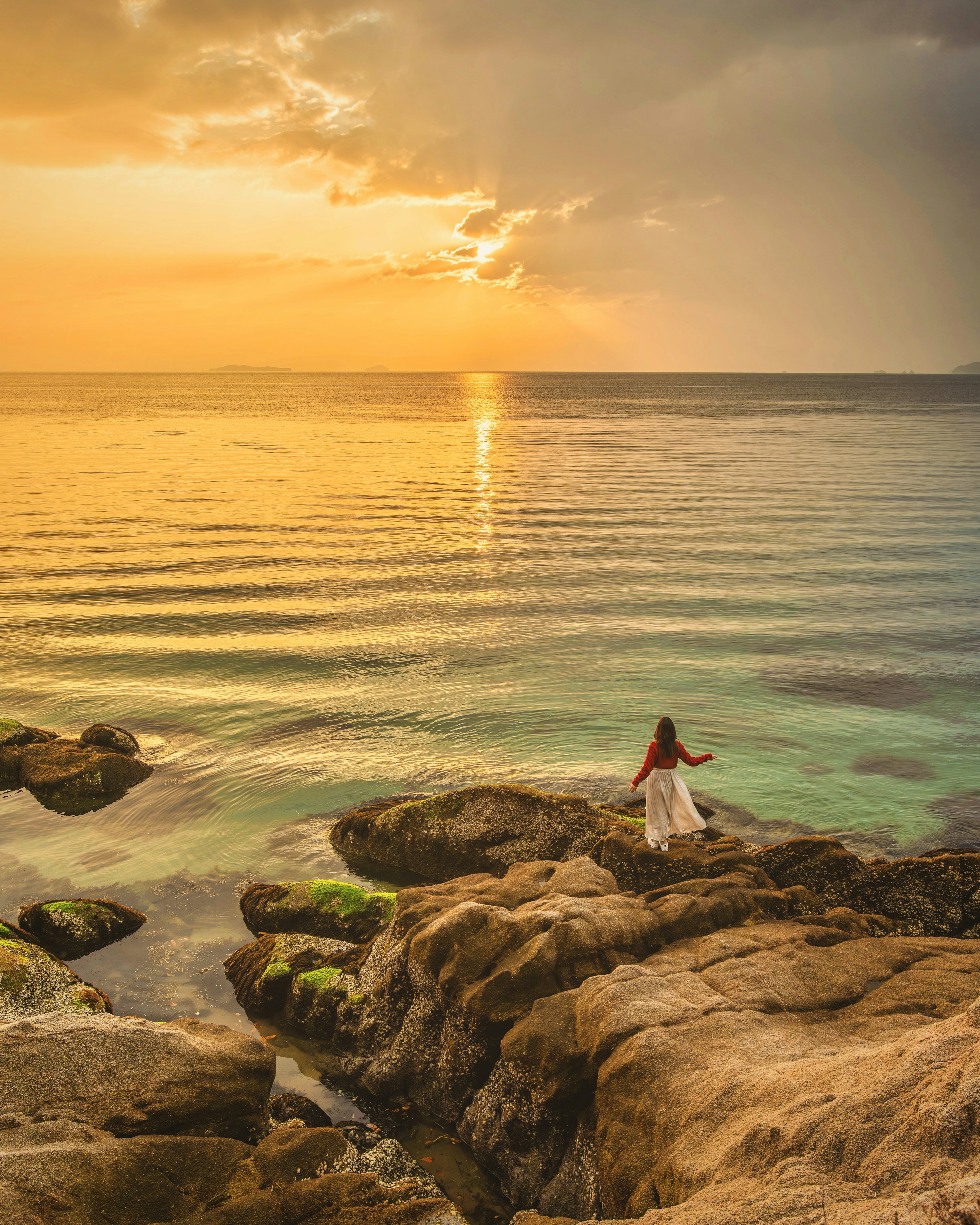 A woman standing on rocks by the sea during a beautiful sunset