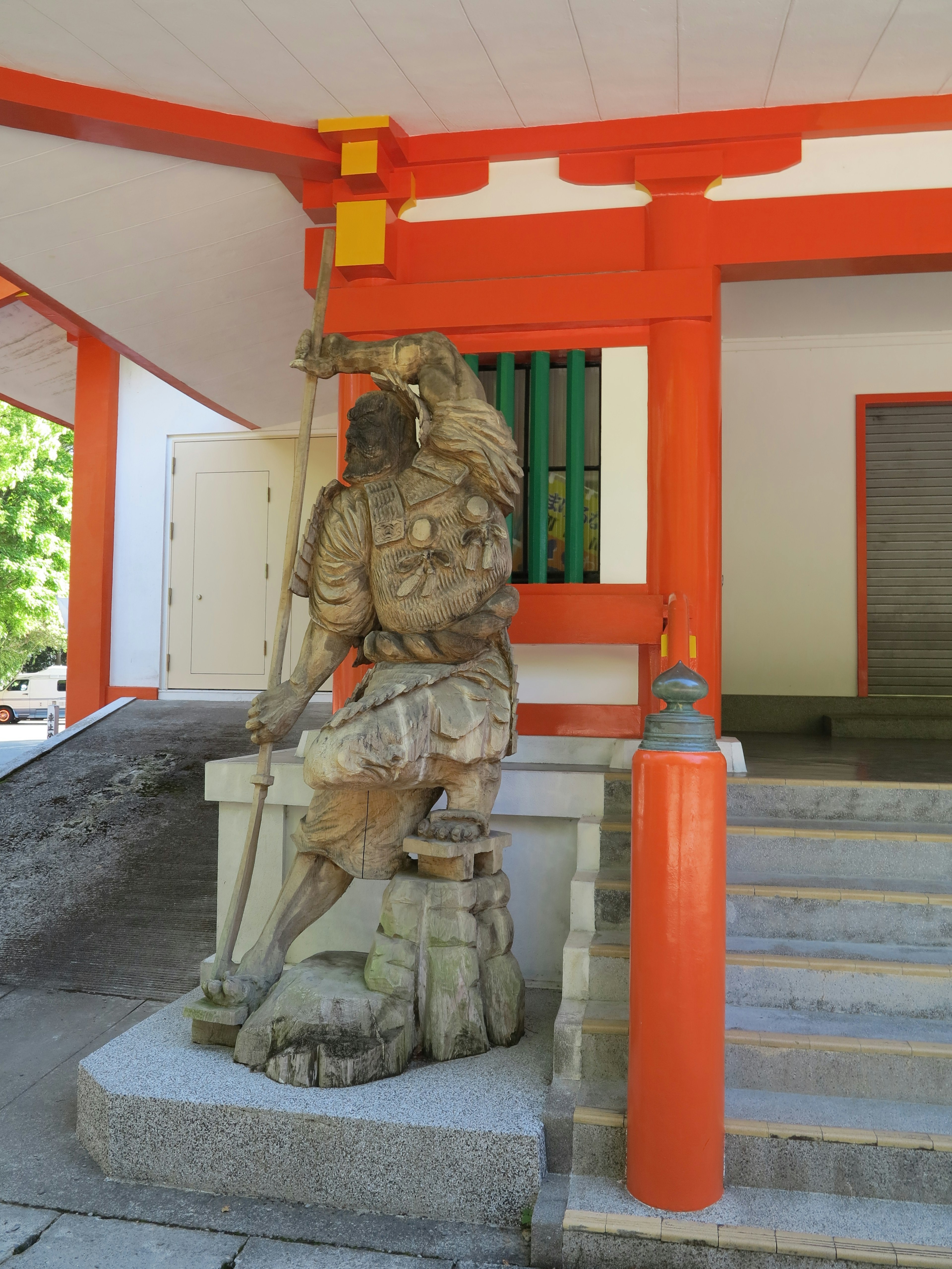 Wooden sculpture of a man holding a staff located in front of a shrine