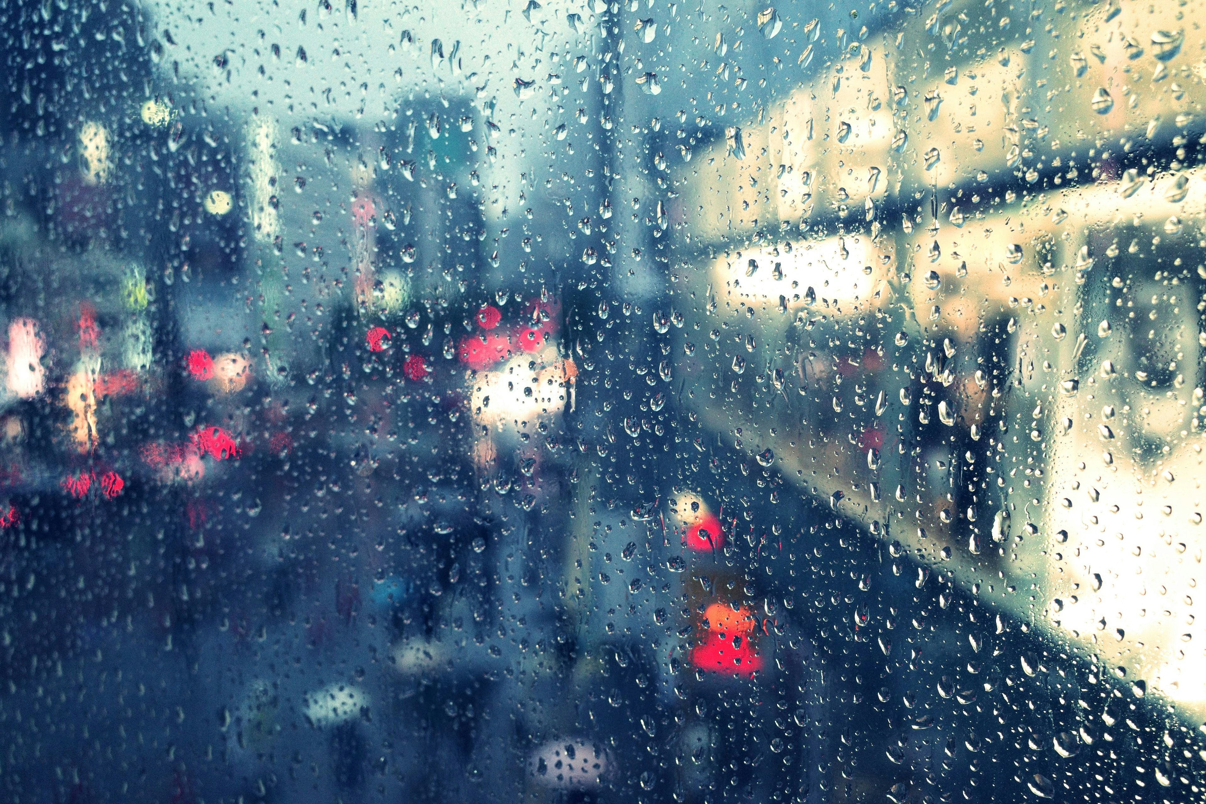 Paisaje urbano visto a través de una ventana empapada de lluvia con luces y colores borrosos