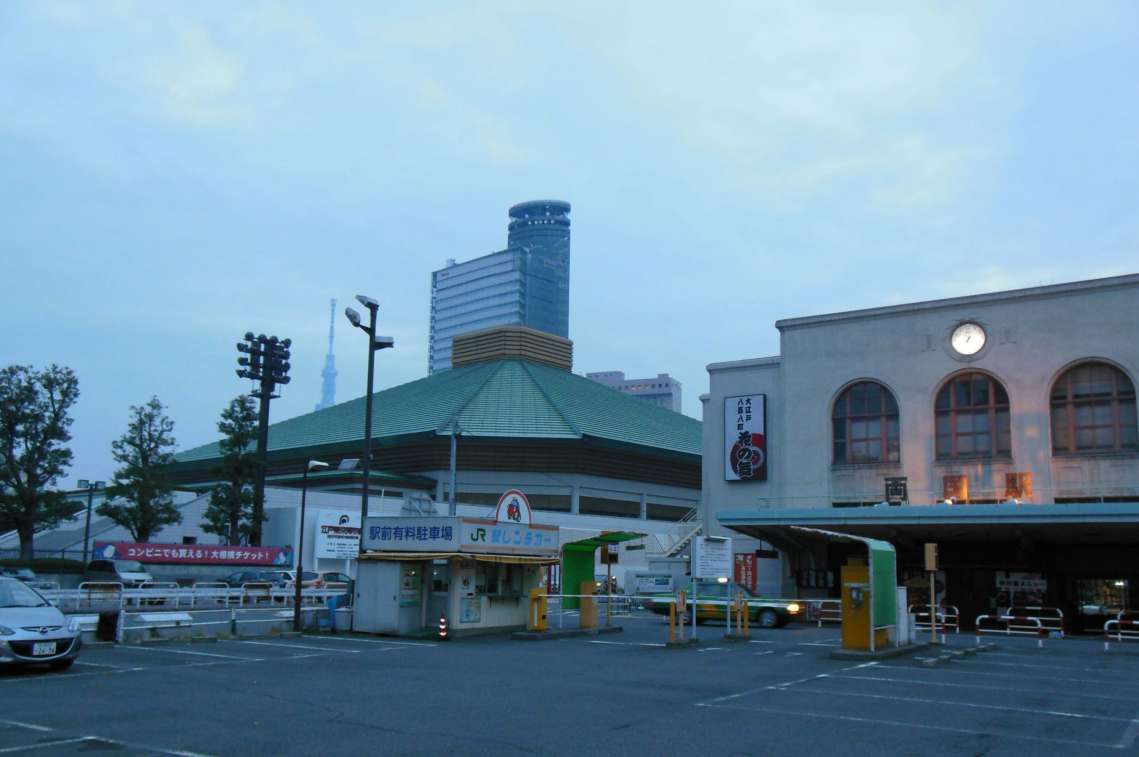 Abendansicht eines Bahnhofsbereichs mit einem Hochhaus und traditioneller Architektur