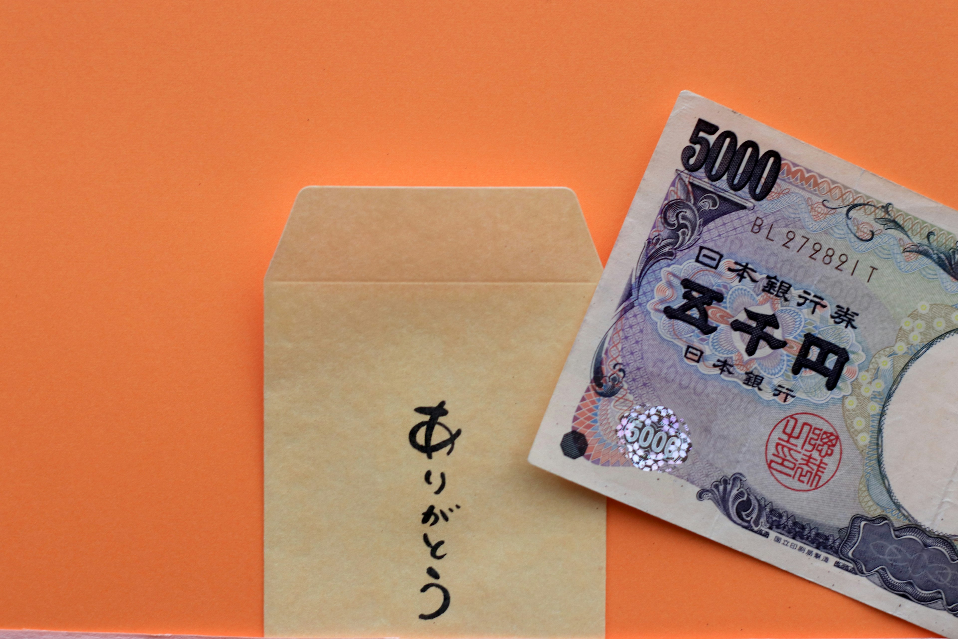 An envelope expressing gratitude next to a 5000 yen note on an orange background