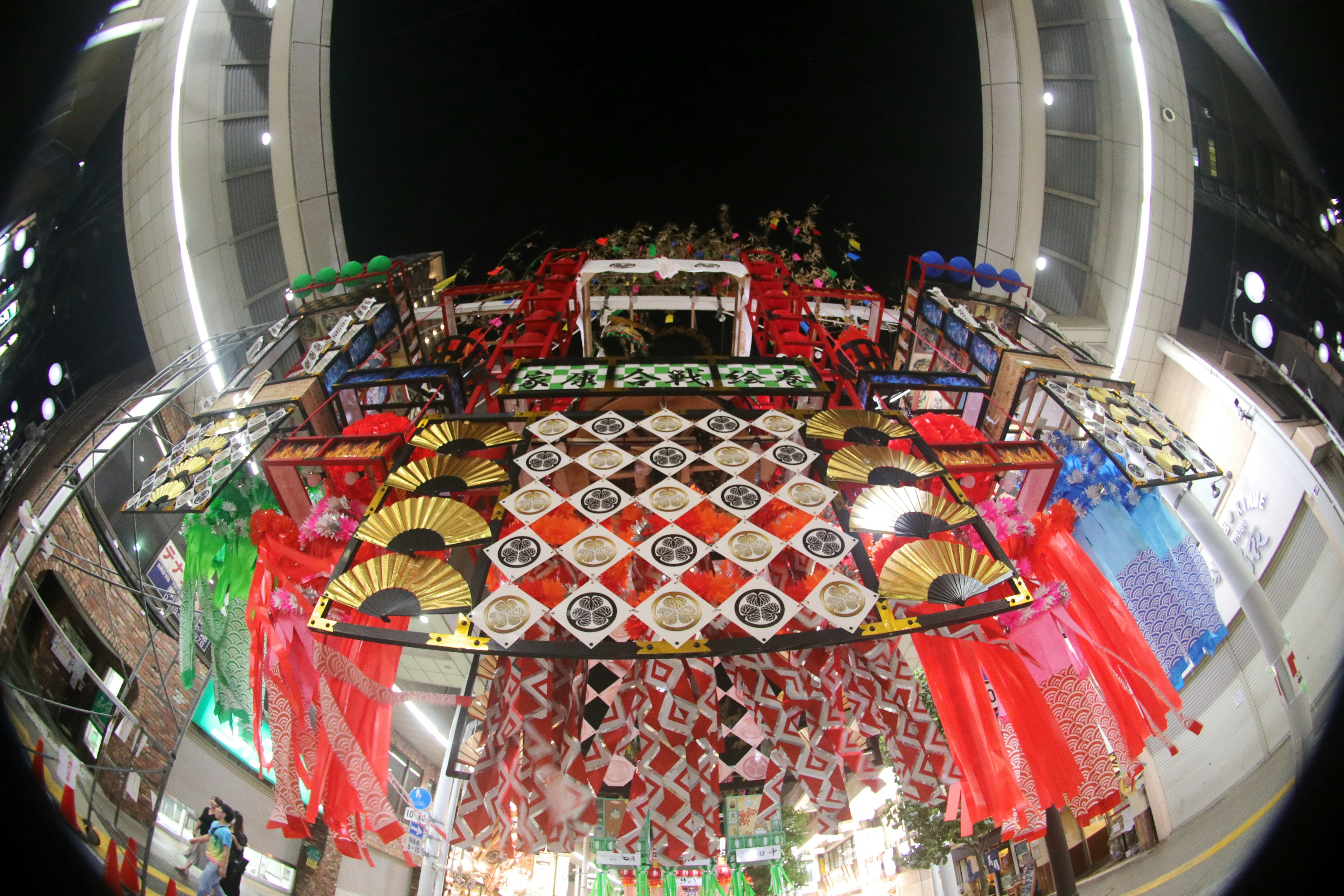 Vue d'en bas d'un stand de festival la nuit avec des décorations colorées et des éventails traditionnels