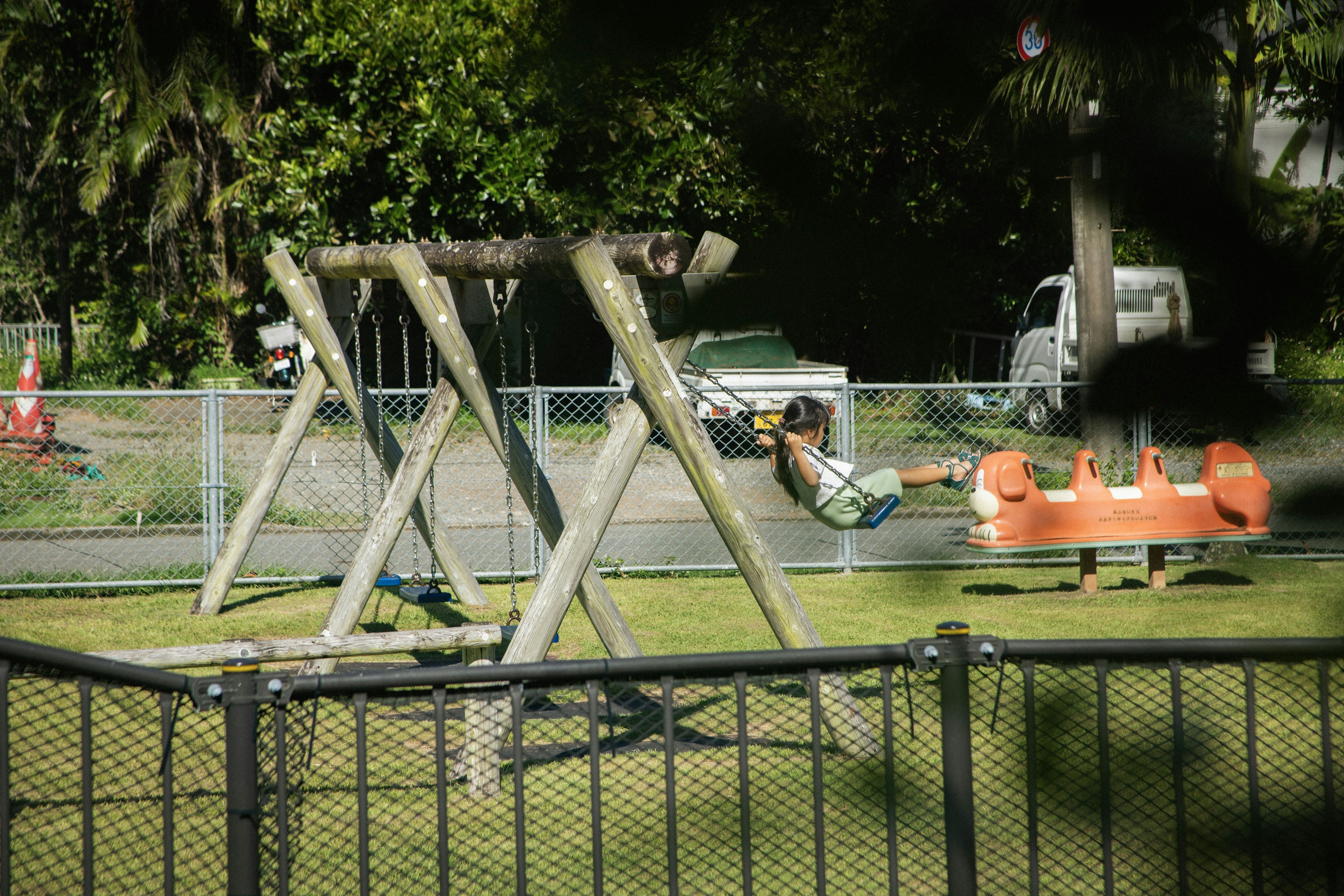 Child playing on a swing in a park with surrounding greenery