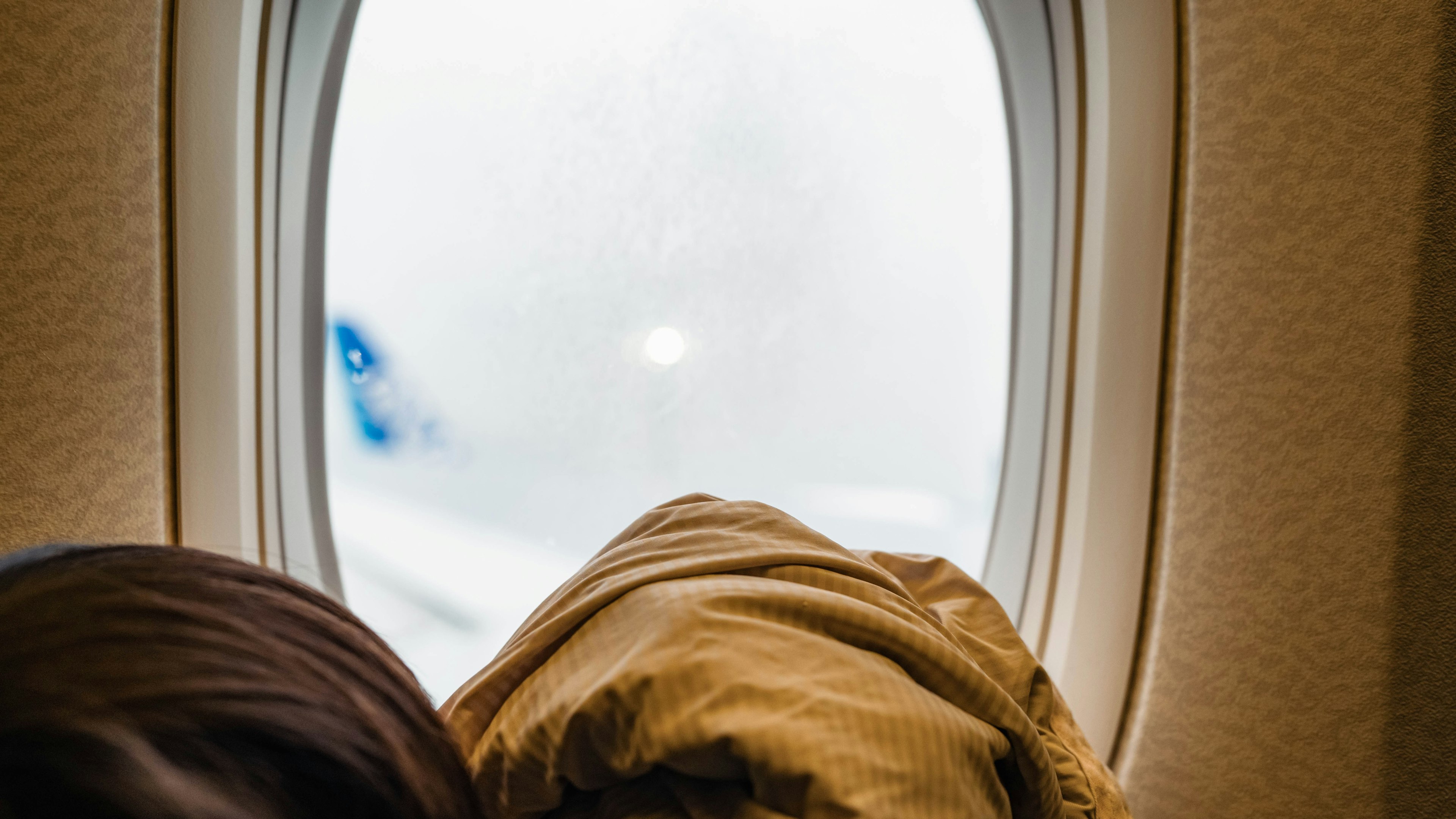 View of a foggy airplane window with a person's head covered in a blanket