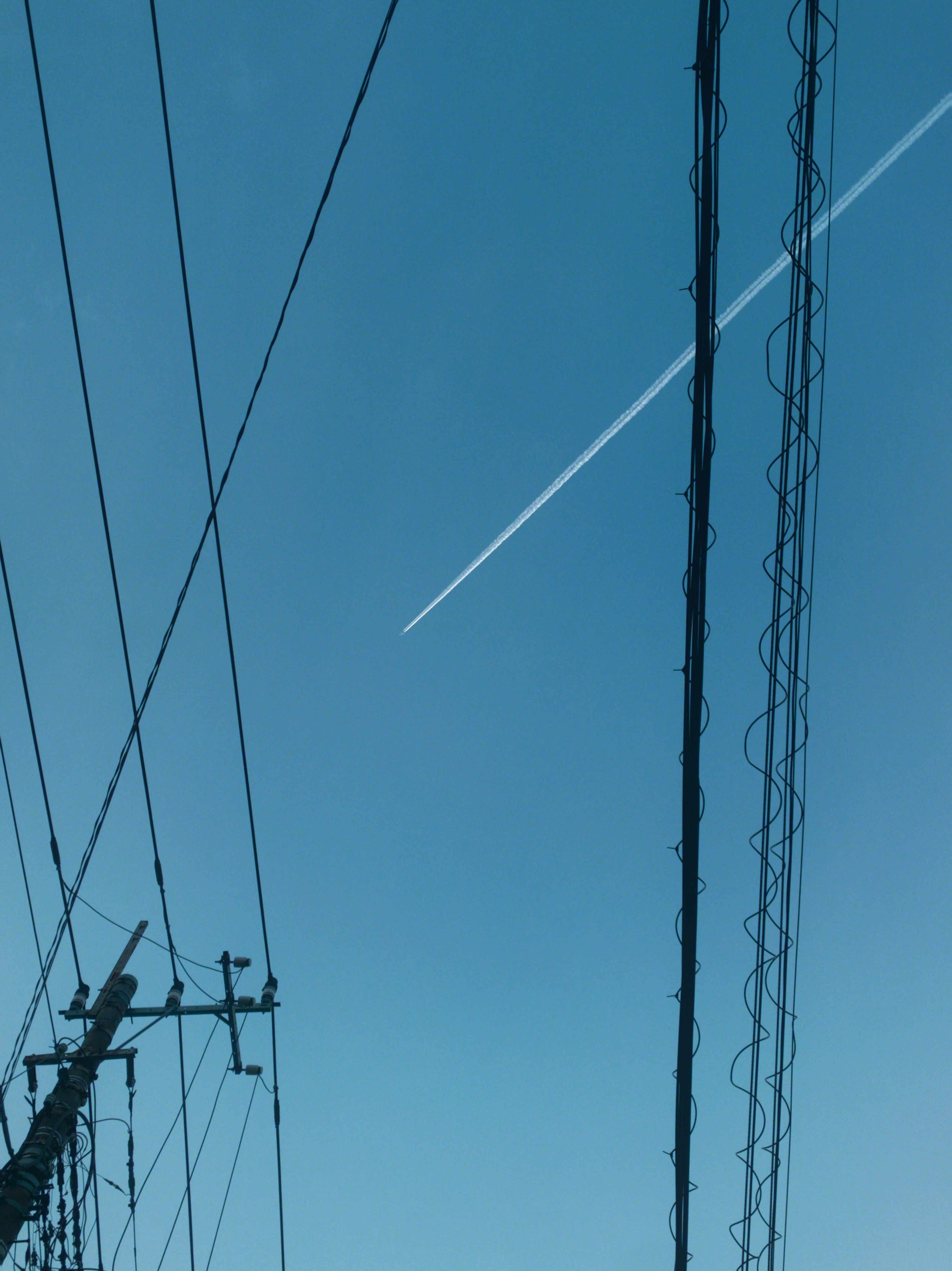 青空に飛行機雲と電線が交差する風景