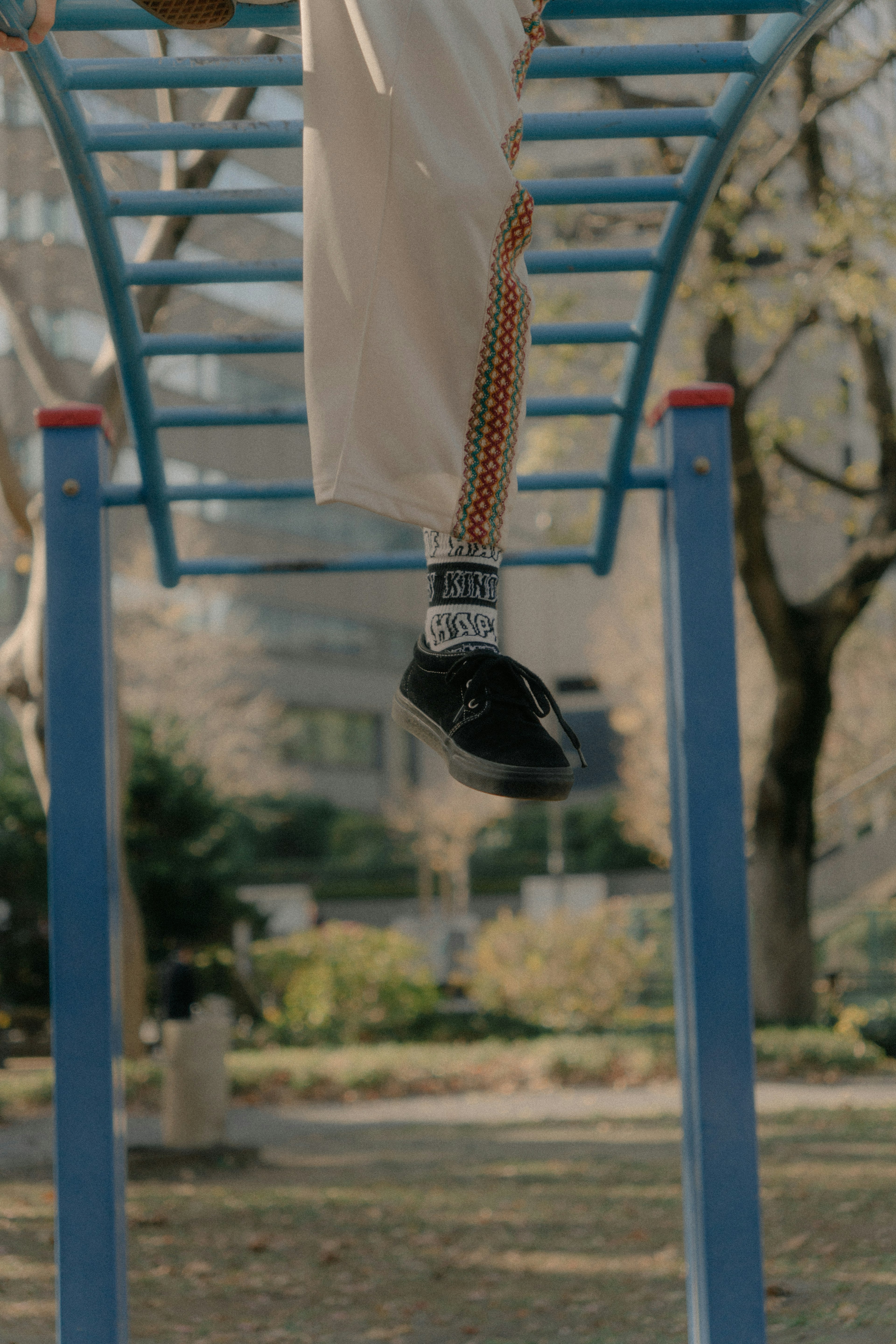 Image de pieds suspendus à une barre de singe bleue dans un parc avec des chaussures noires et des chaussettes blanches