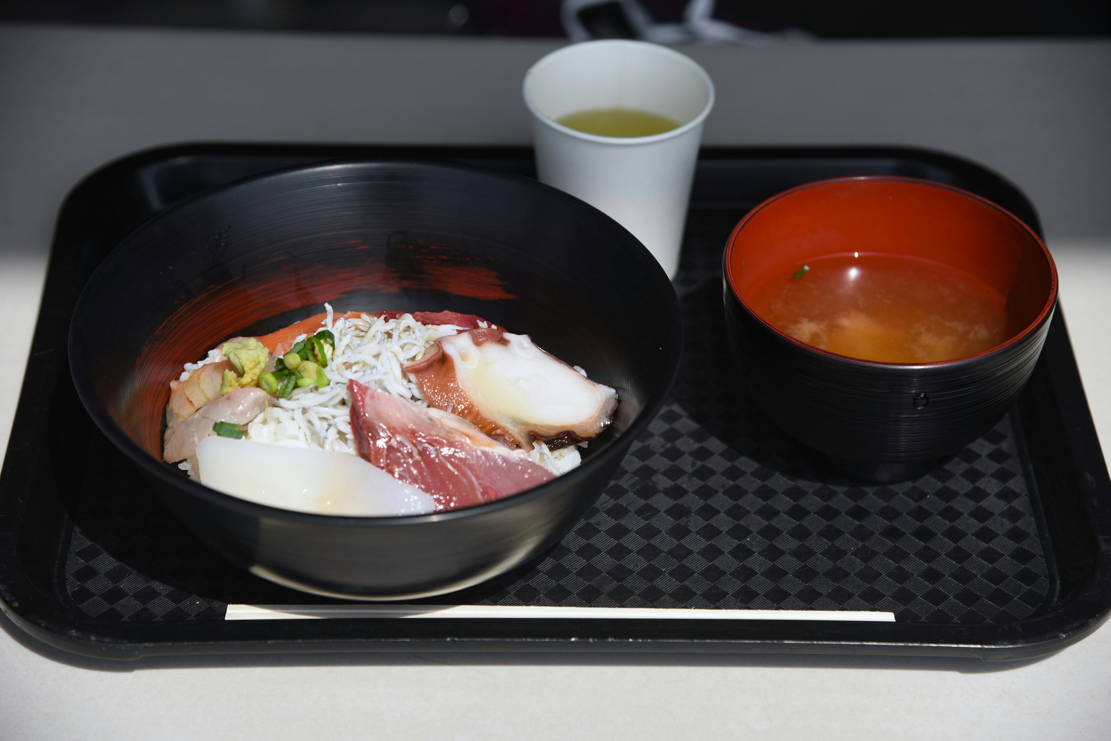 Un plateau avec un bol de riz garni de poisson frais et une tasse de soupe miso