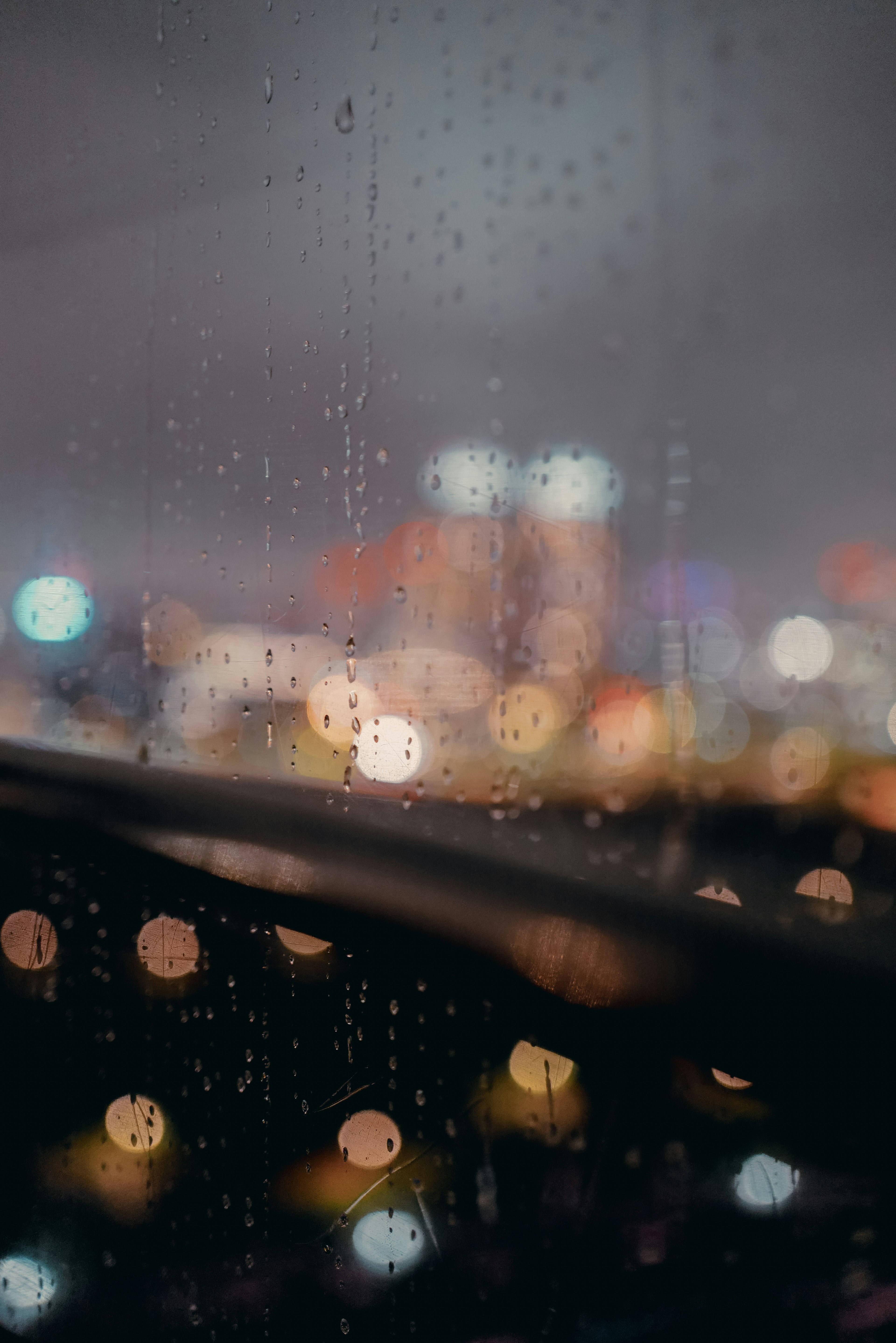 雨滴が付いた窓越しにぼんやりとした都市の夜景が見える