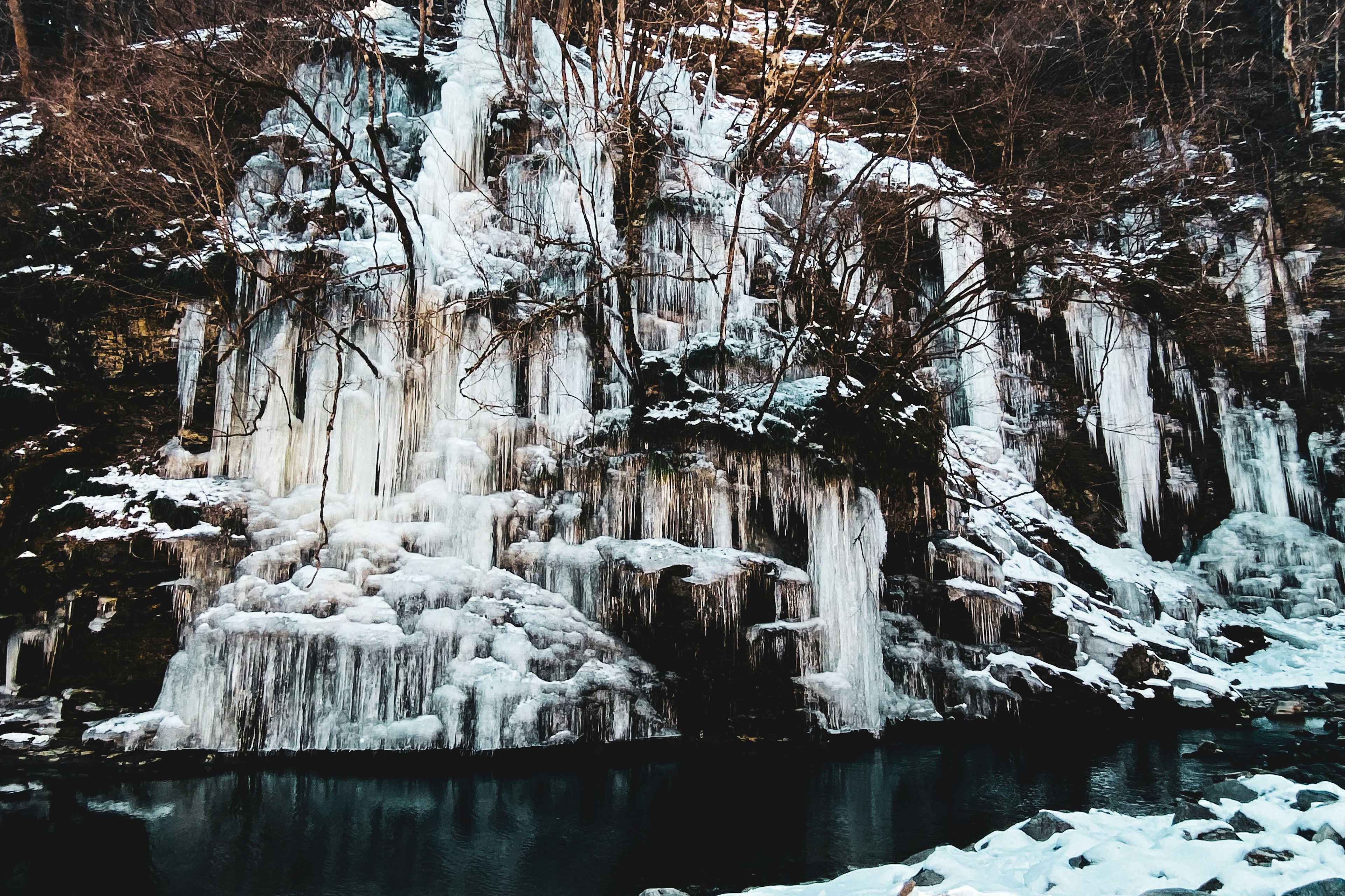 Paesaggio invernale con parete rocciosa coperta di ghiaccio e superficie d'acqua calma