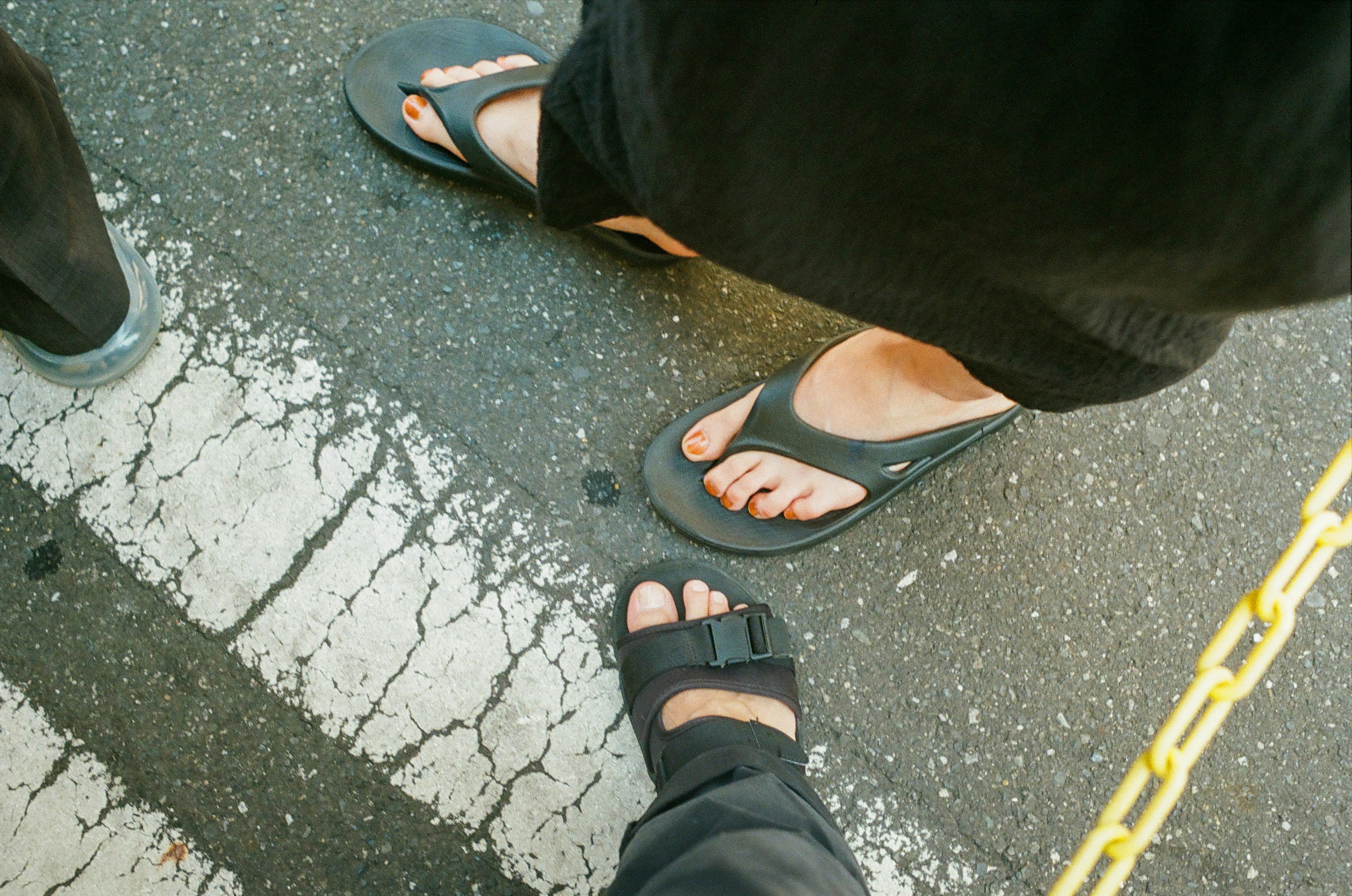 Image showing two pairs of feet wearing sandals and flip-flops on a cracked pavement