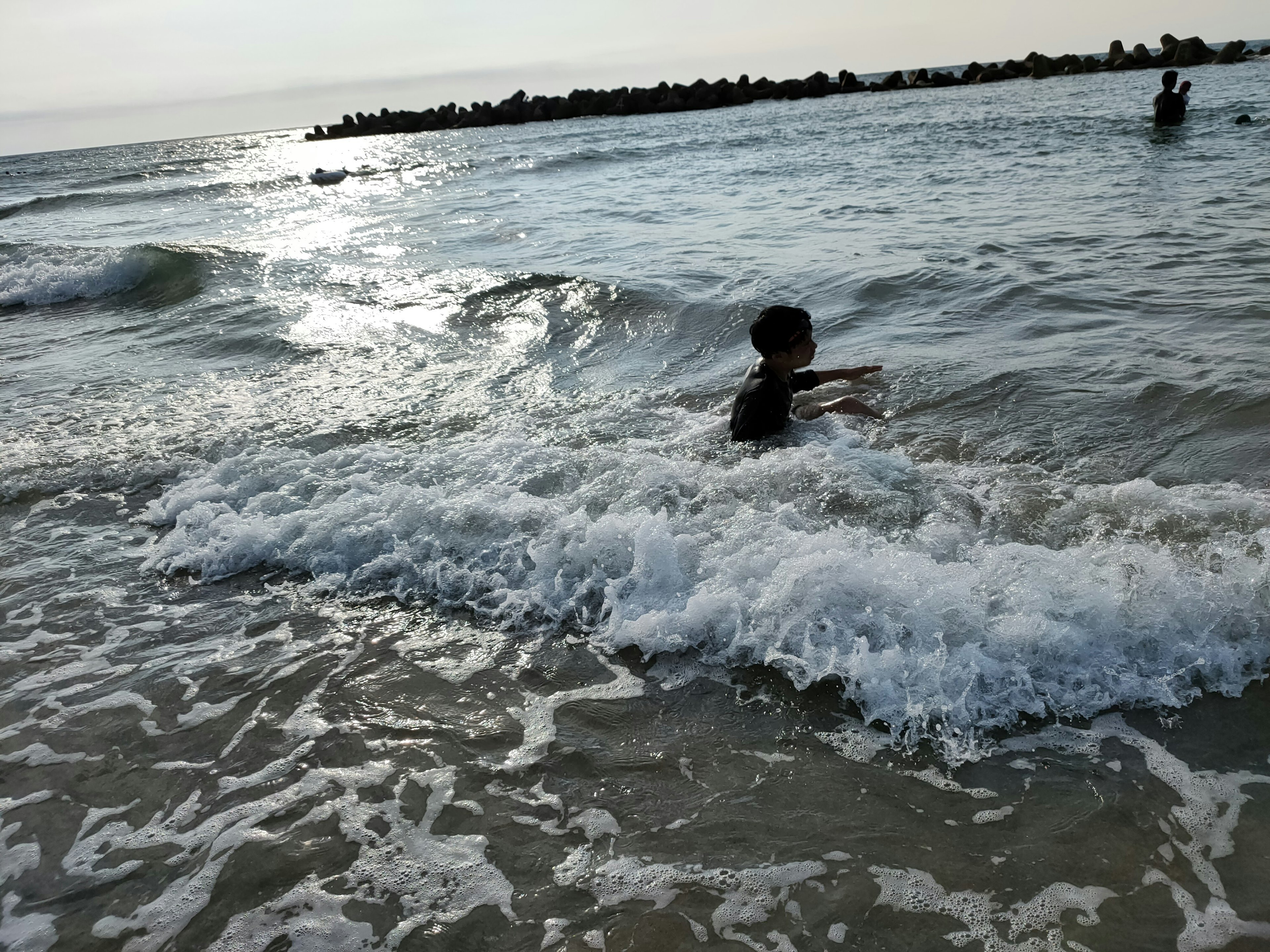 Kind spielt im Meer mit Wellen und Sonnenlicht, das auf das Wasser reflektiert